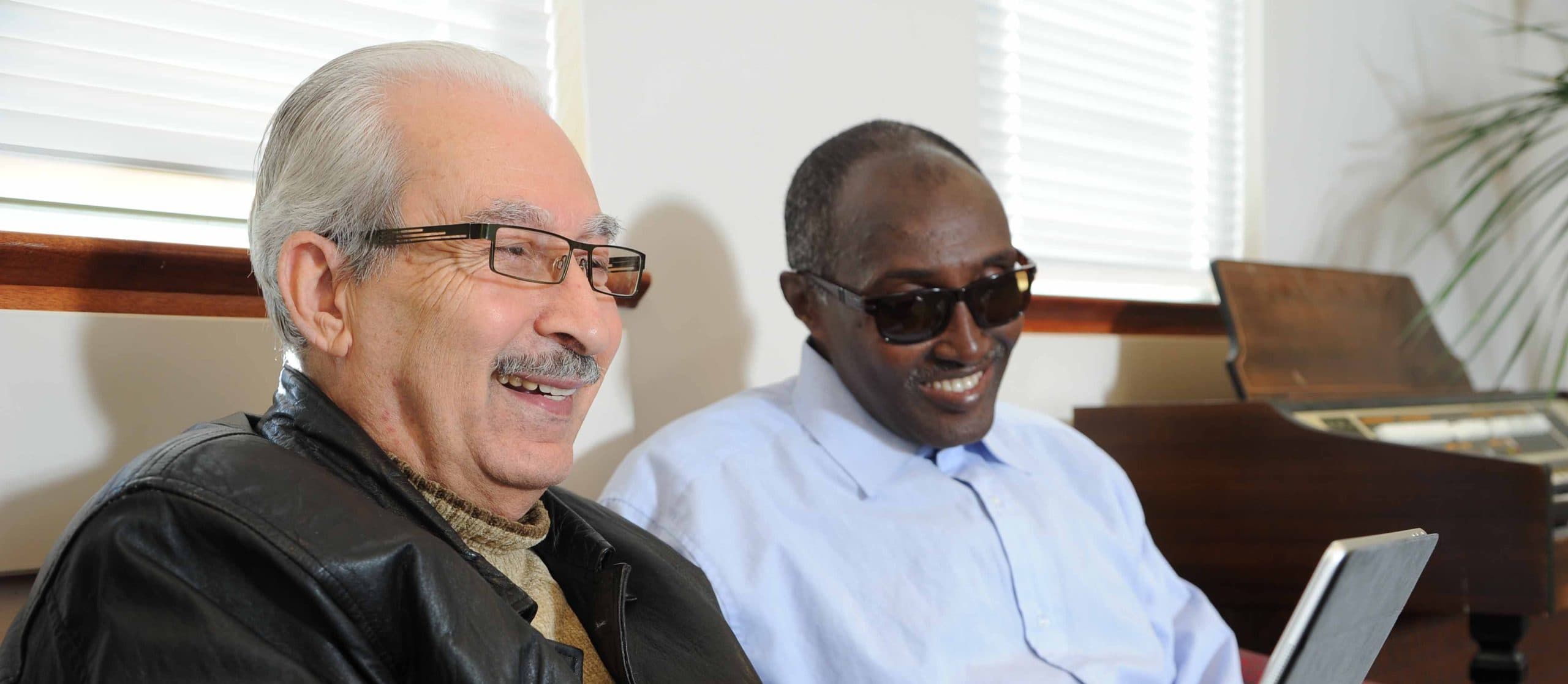 Two older male cllients share a laugh, one of them is using a tablet