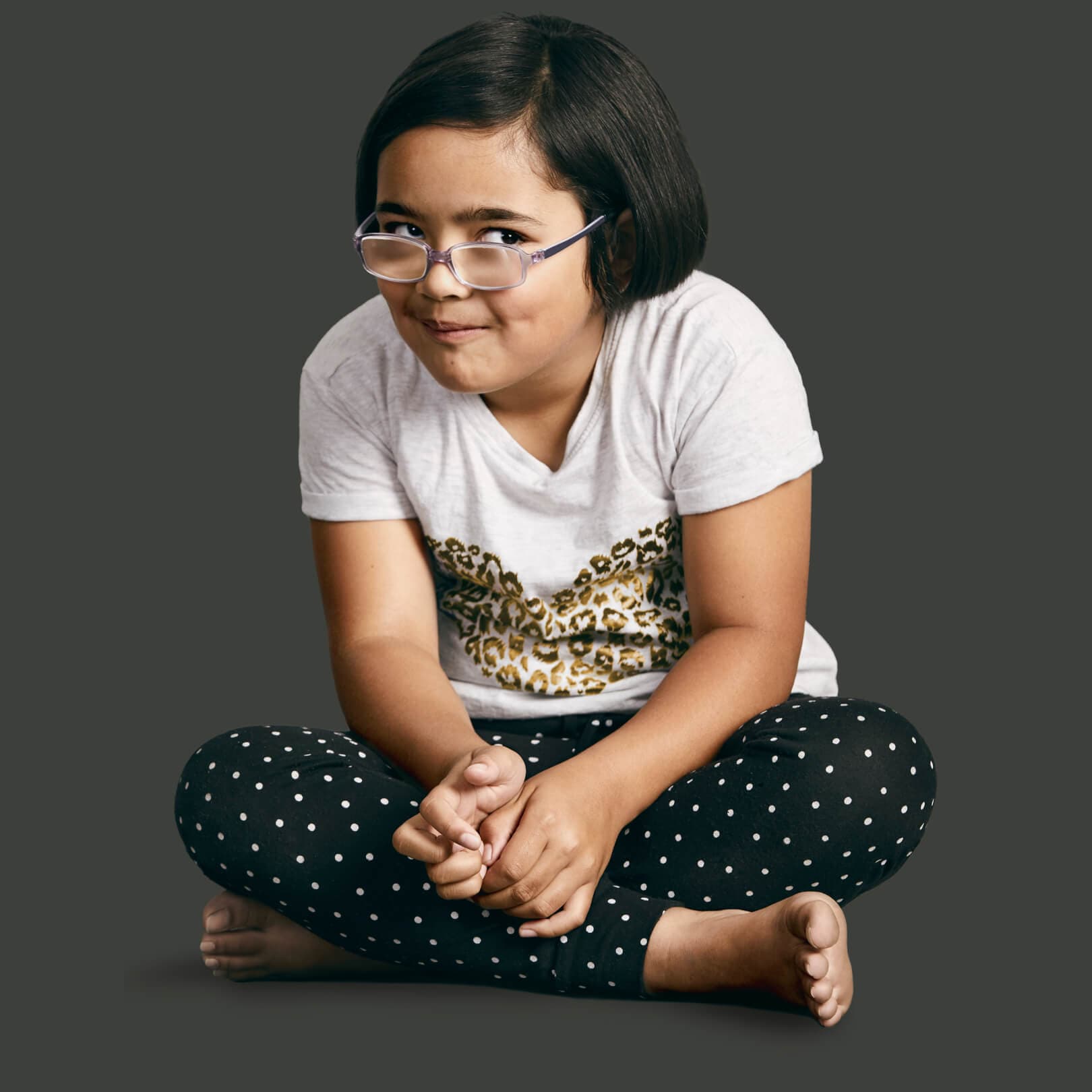 Young client Tara, looks cheekily at the camera as she sits cross-legged on the floor