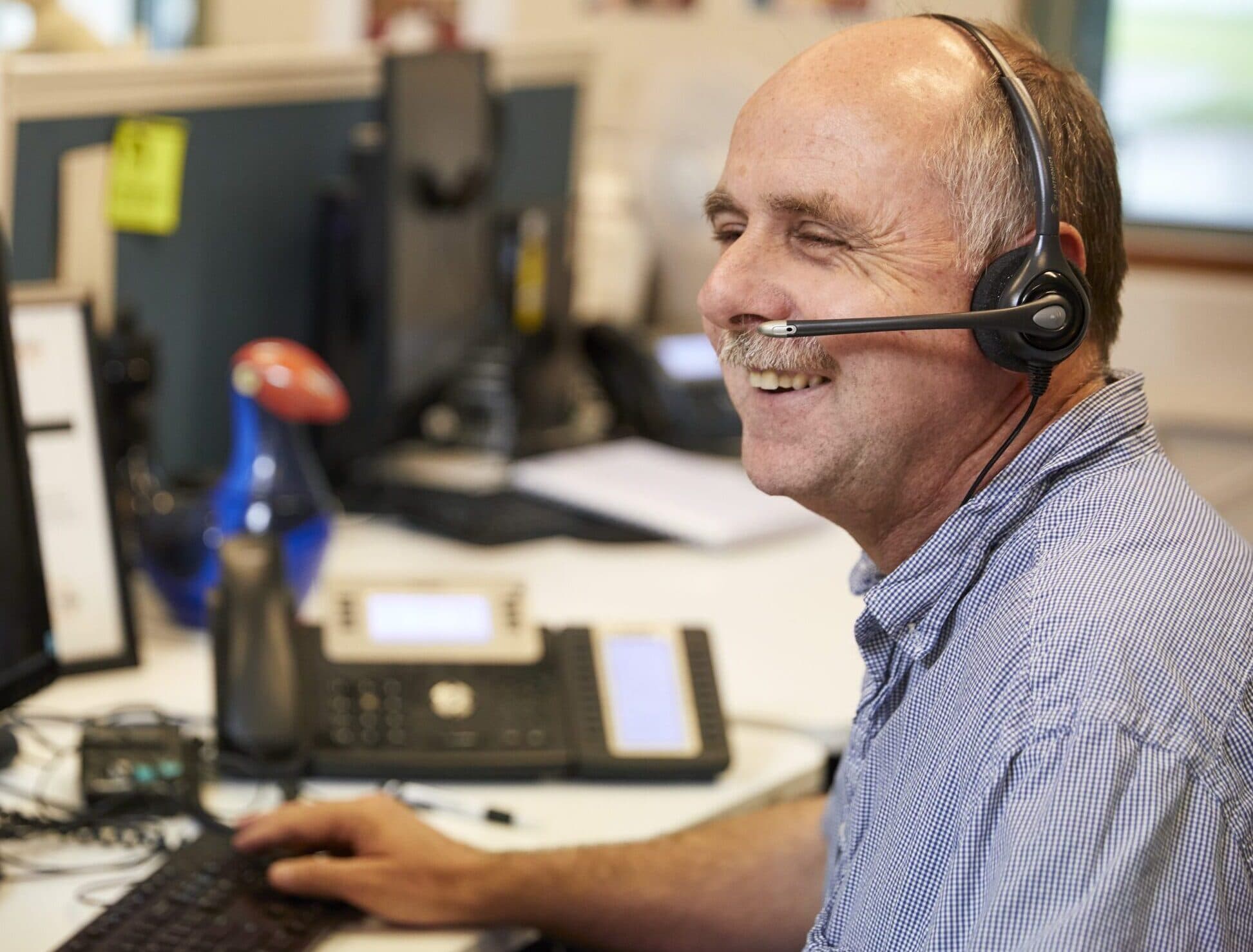 Blind Low Vision NZ staff member Ivan is sitting at his computer and answering donor enquiries