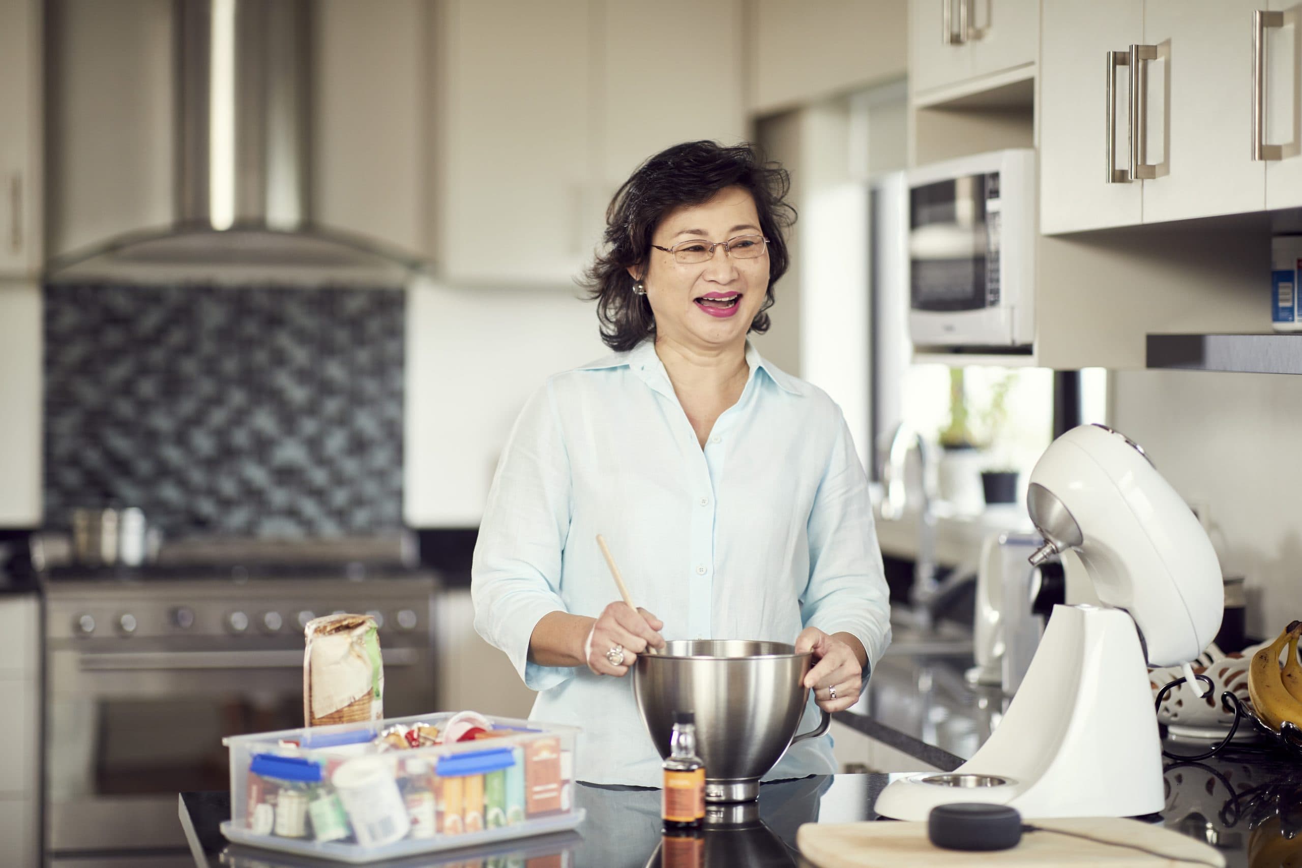 Client Karen stands in her kitchen baking with a huge smile on her face