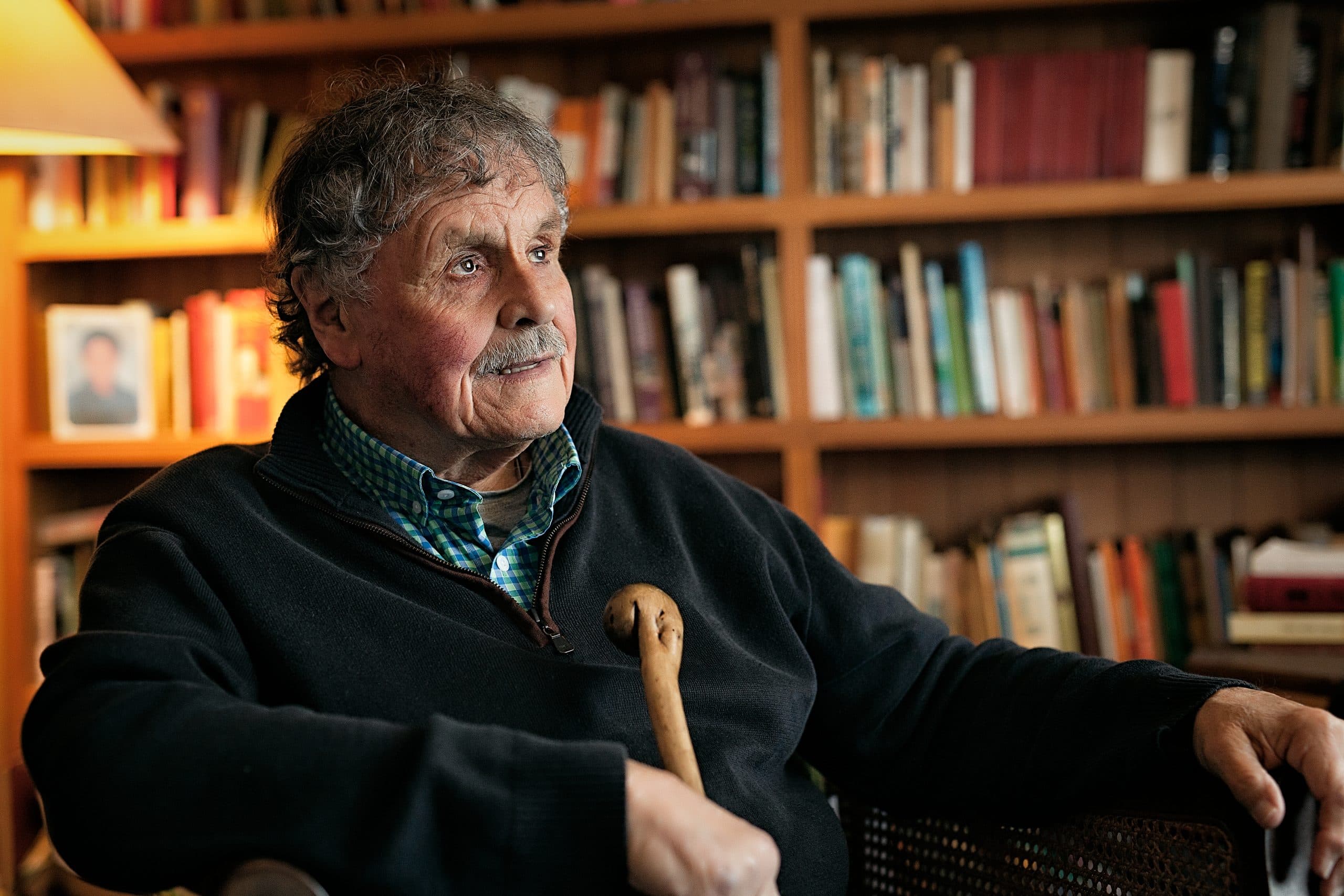 Client Dean sits comfortably in front of shelves full of books. He looks off to the right hand side.