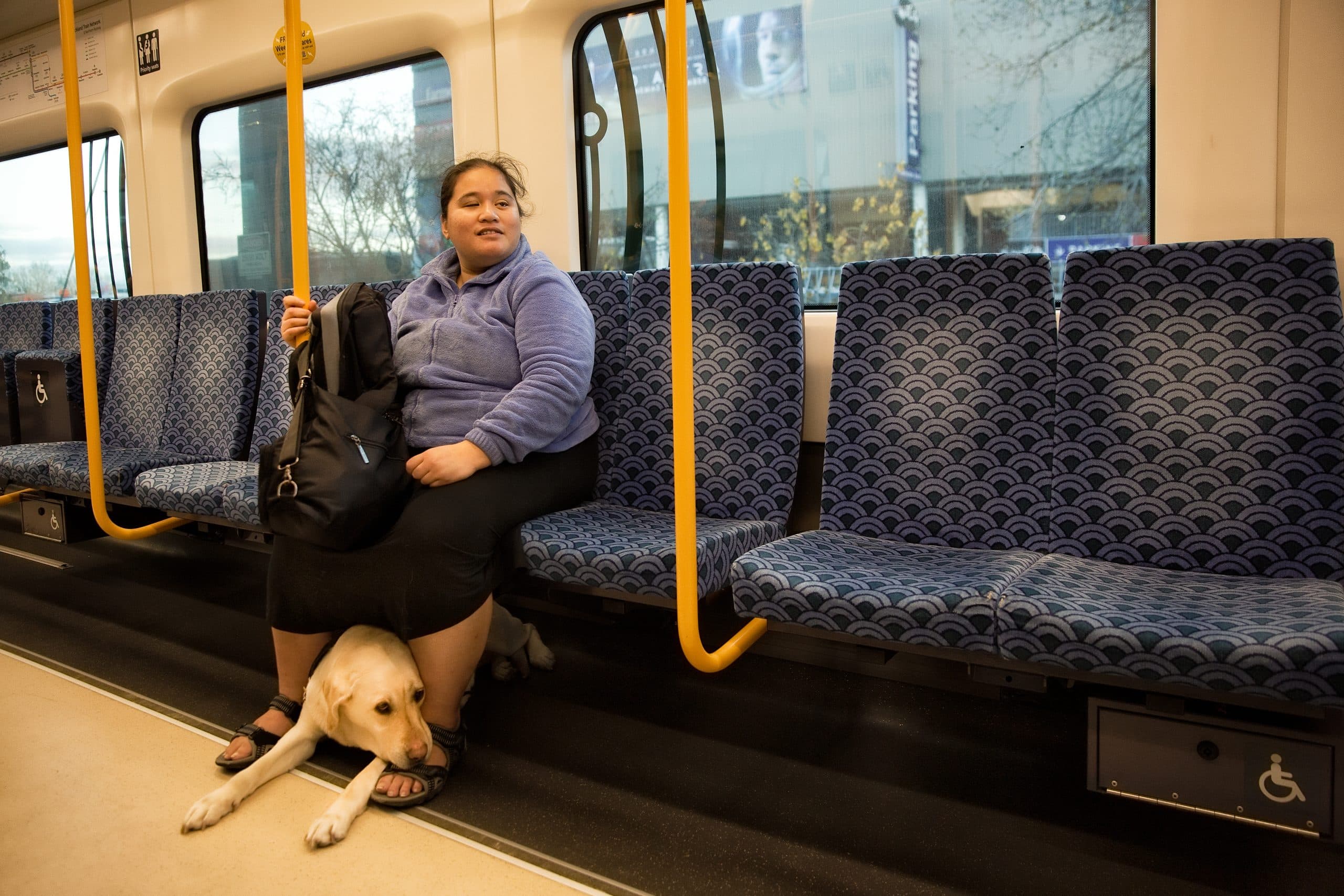 Sina and her guide dog are sitting on a train as she travels to work.