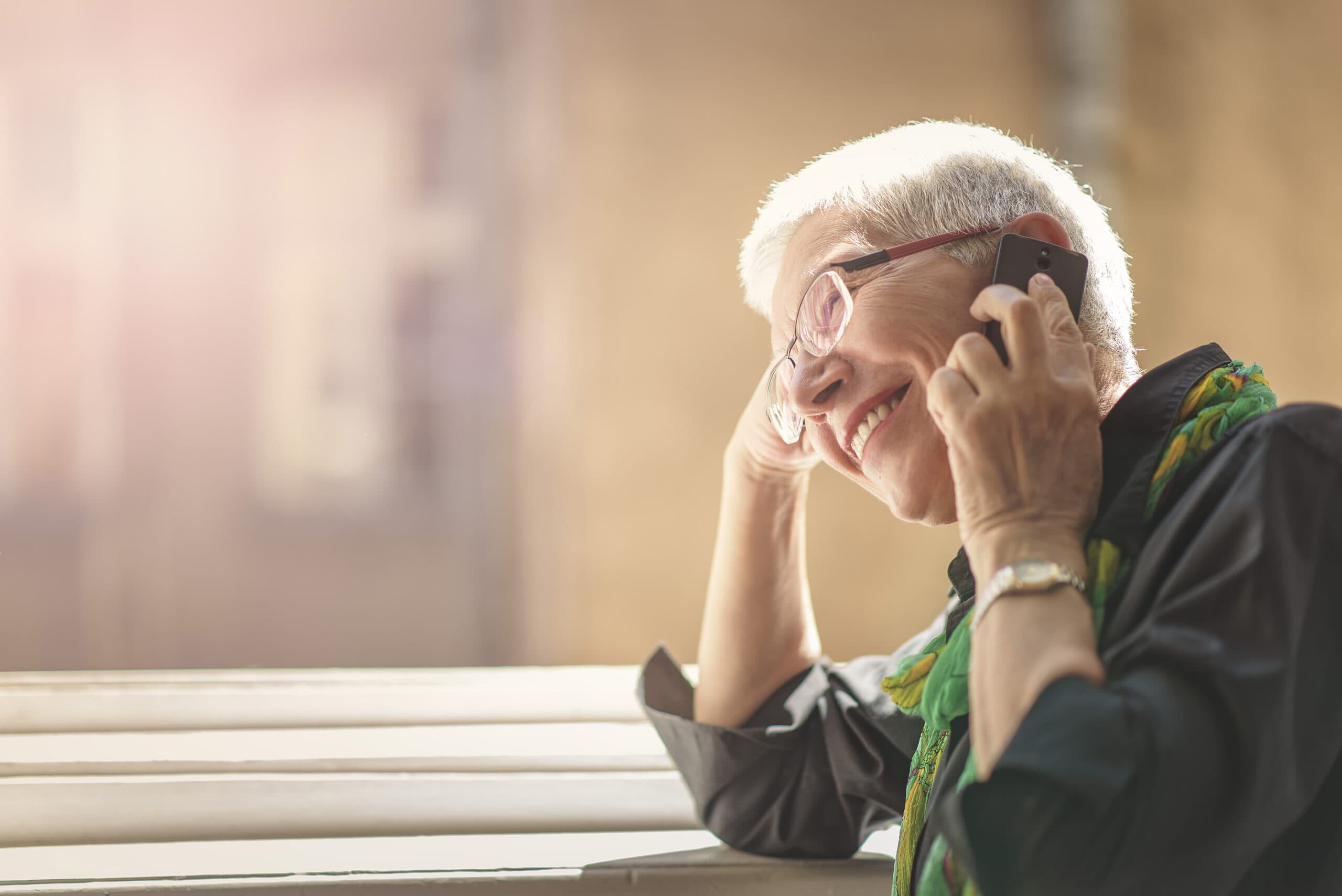 An older woman is sitting at a bench and talking on the phone