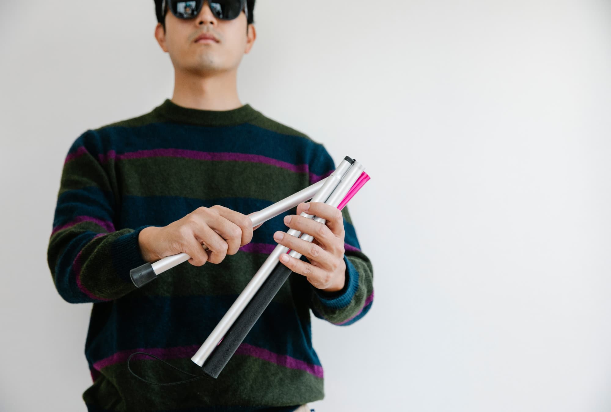 A blind or low vision man holding his unassembled white cane