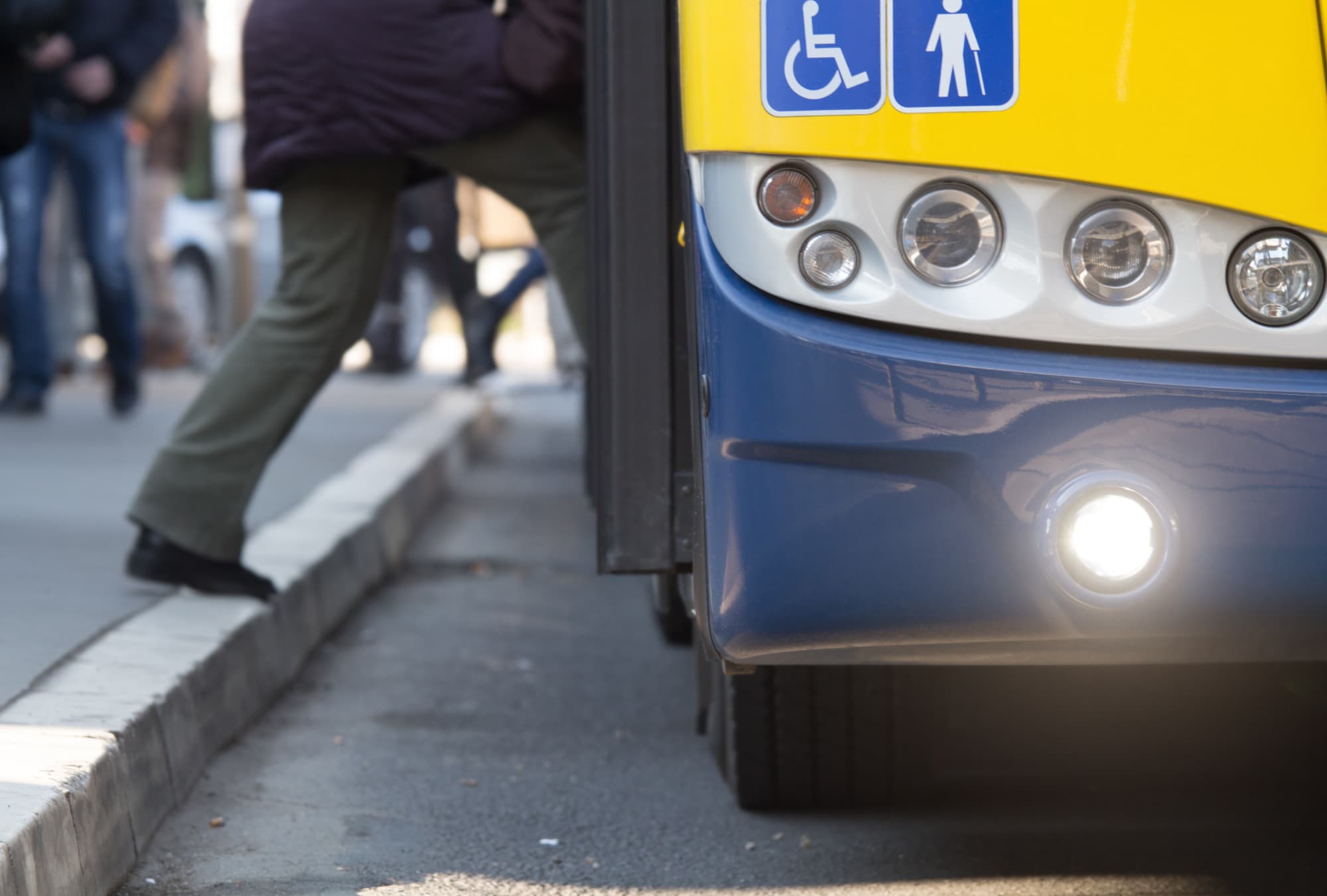 A zoomed in picture of a man onboarding a bus. The bus has two accessibility stickers.