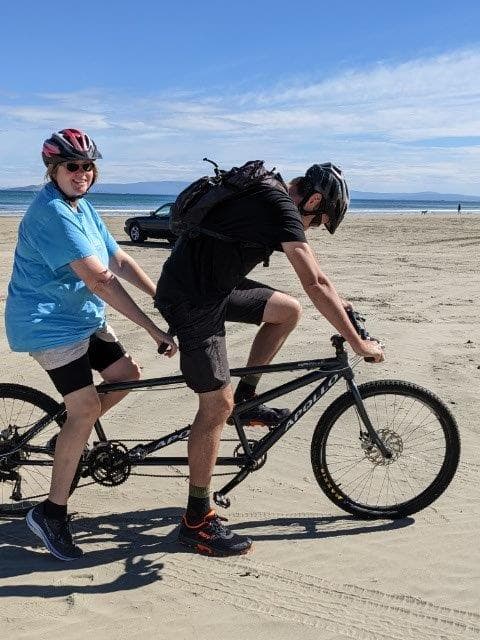 A female client enjoys a tandem bike ride through Oreti Beach