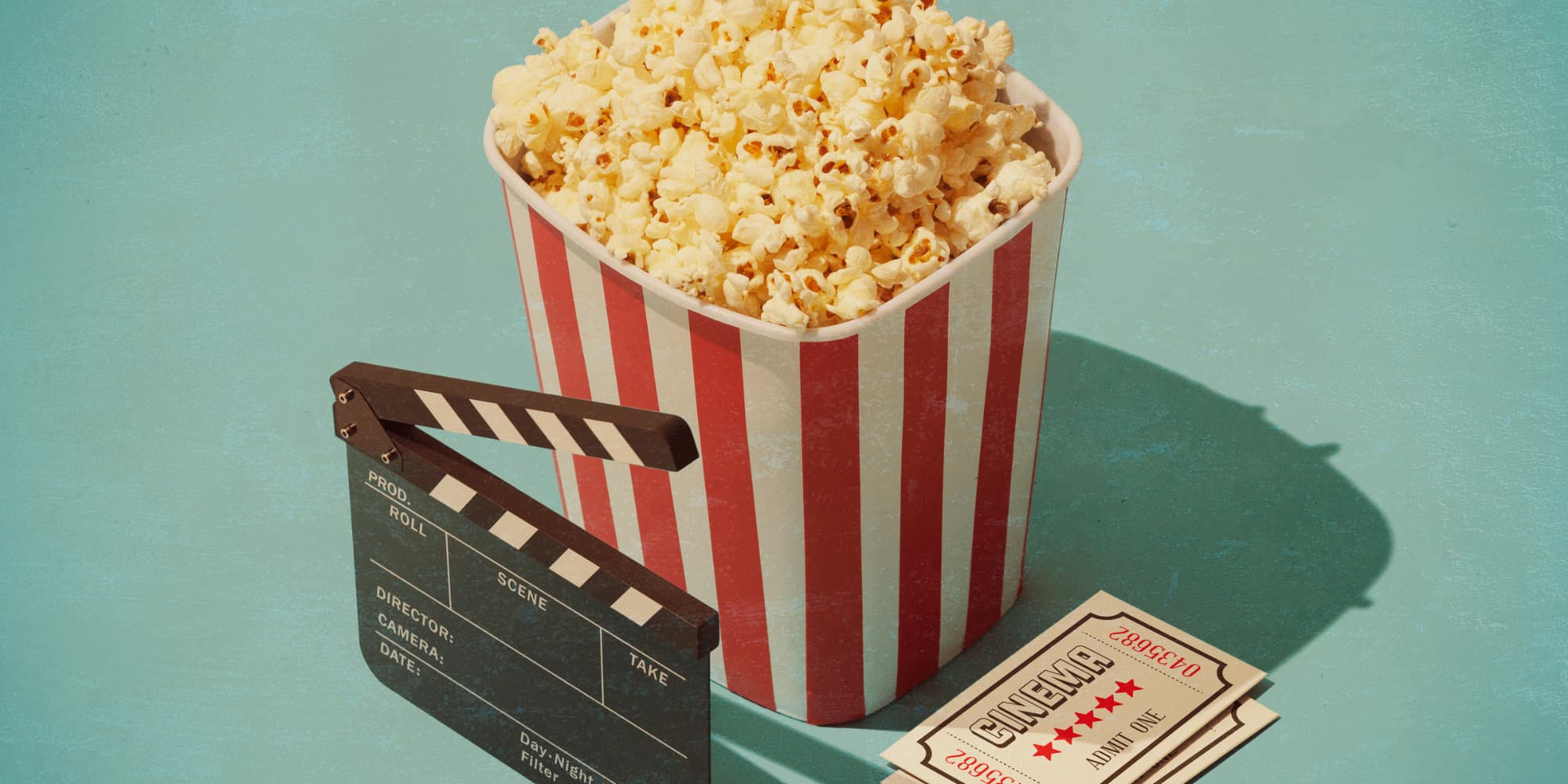A box of popcorn, a movie clapboard and two cinema tickets displayed on a teal surface.