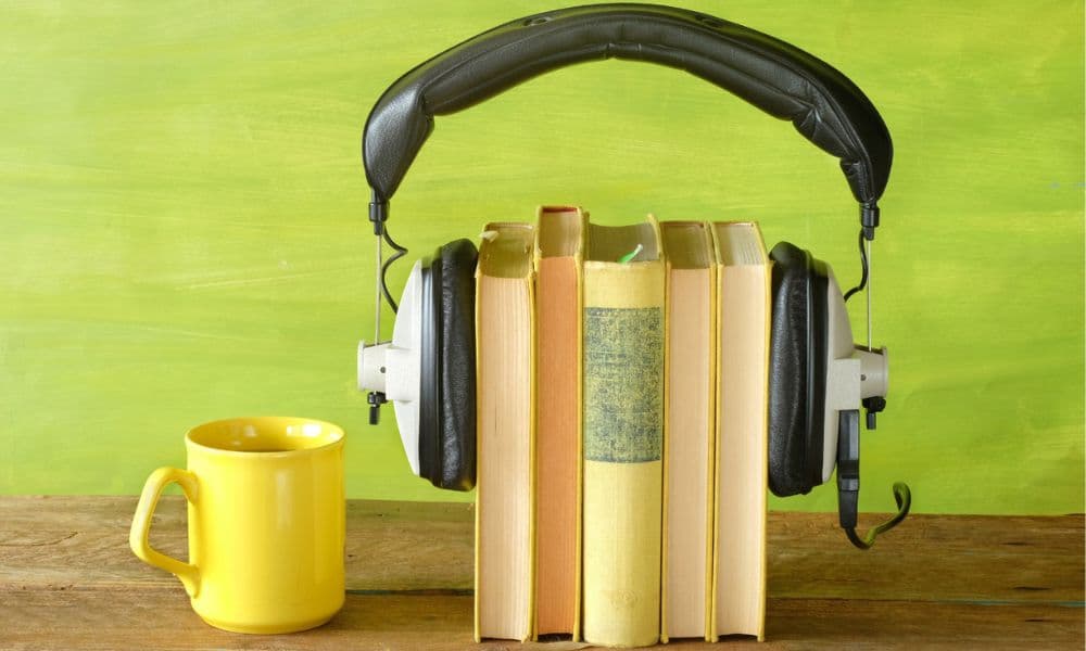 Five books standing upright on a table, wearing headphones and sitting next to a yellow cup.