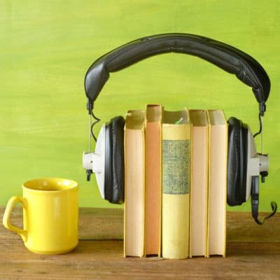 A graphic of a stack of books using a headset as a pair of bookends. A yellow mug is positioned next to the books on a wooden table.