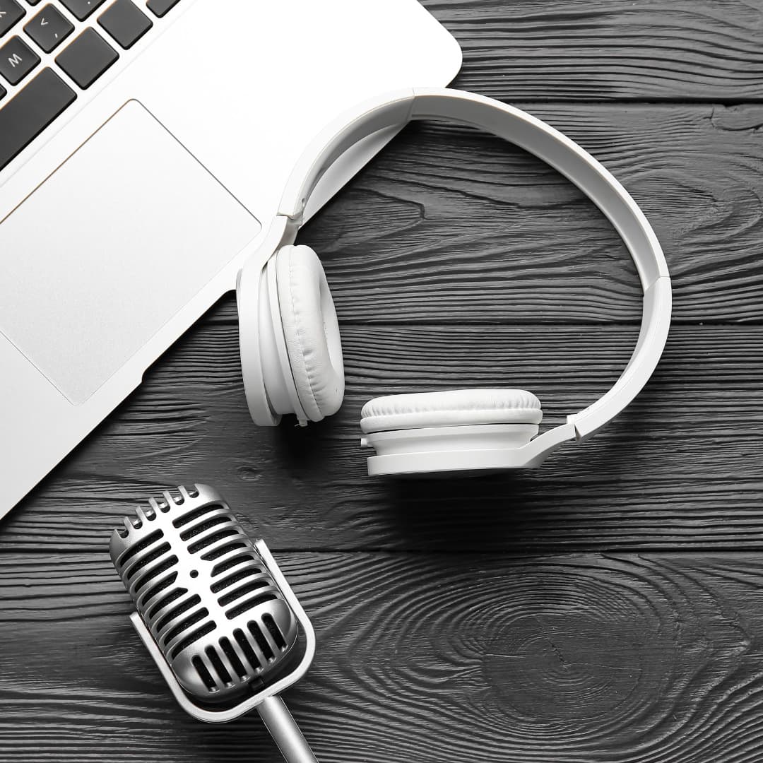 An image of a desk top with headphones, a microphone, and a laptop computer.
