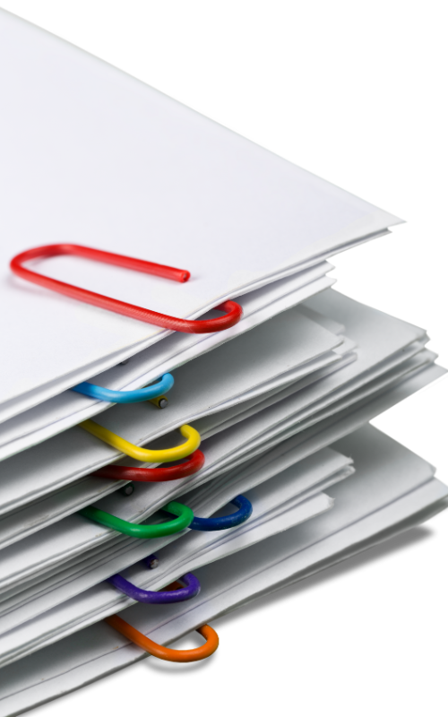 A pile of reports, each one is bound with a coloured paperclip.