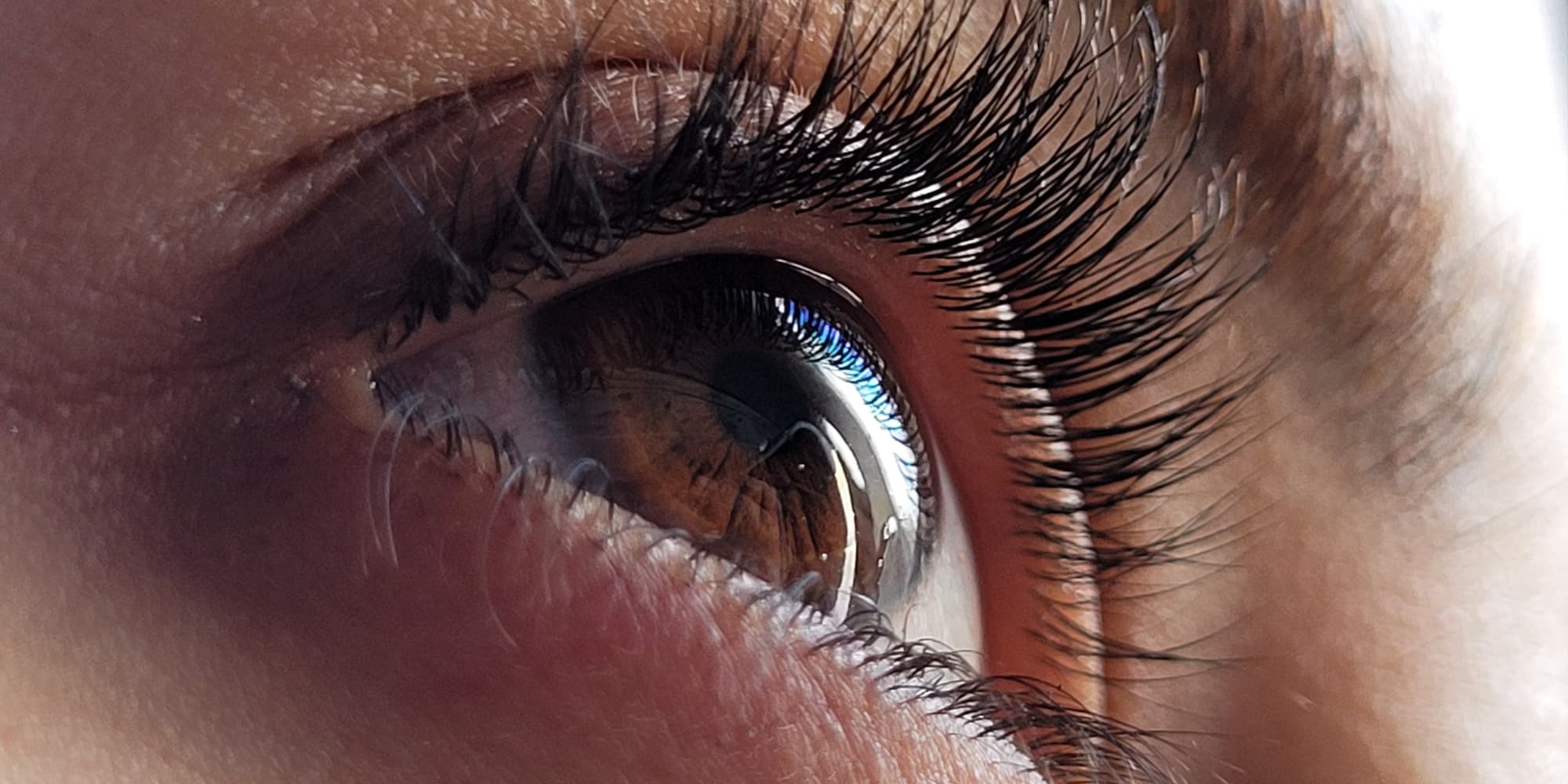 A close up of a human eye looking upwards with light reflecting in it.