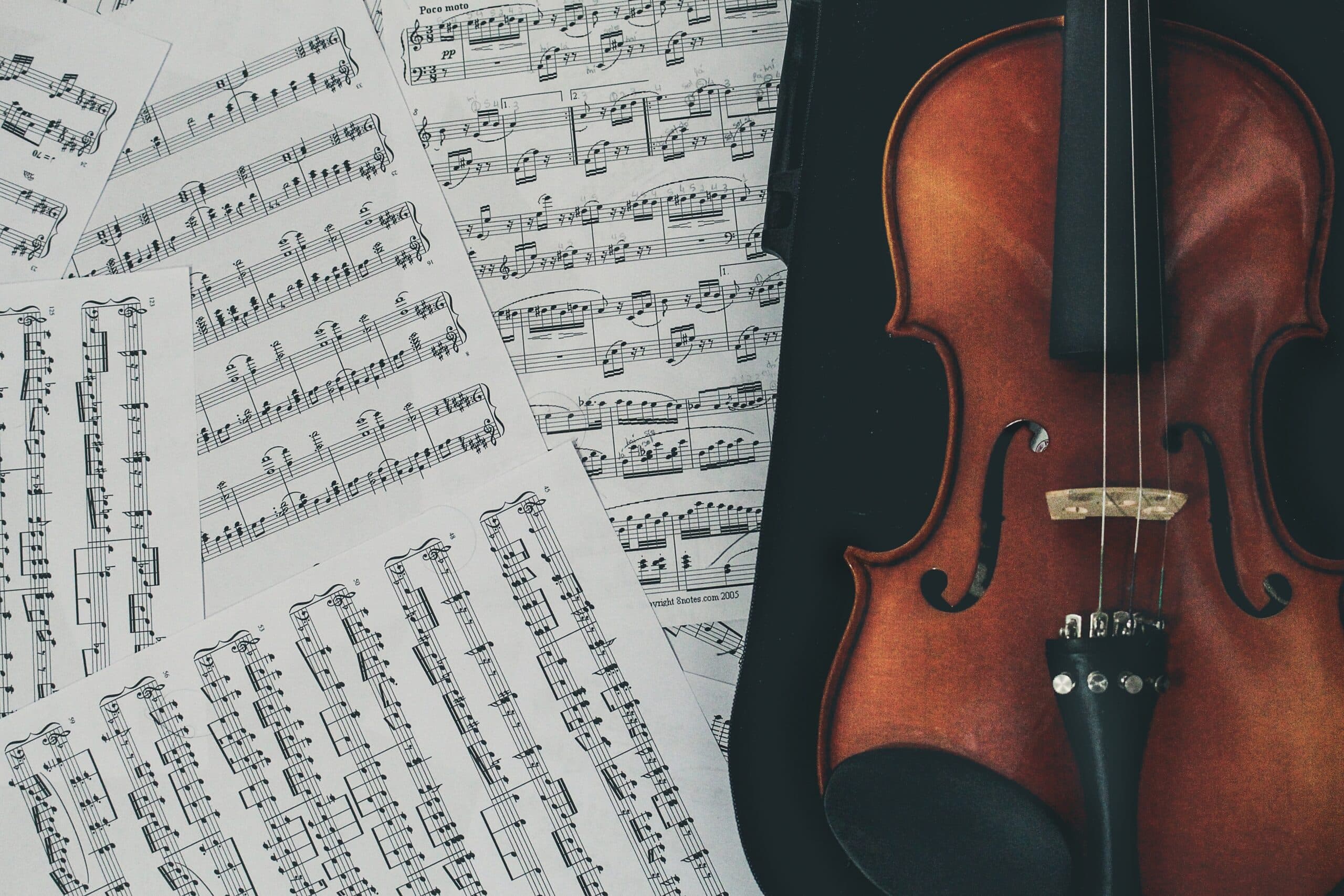 Several pages of sheet music placed next to a shiny violin.