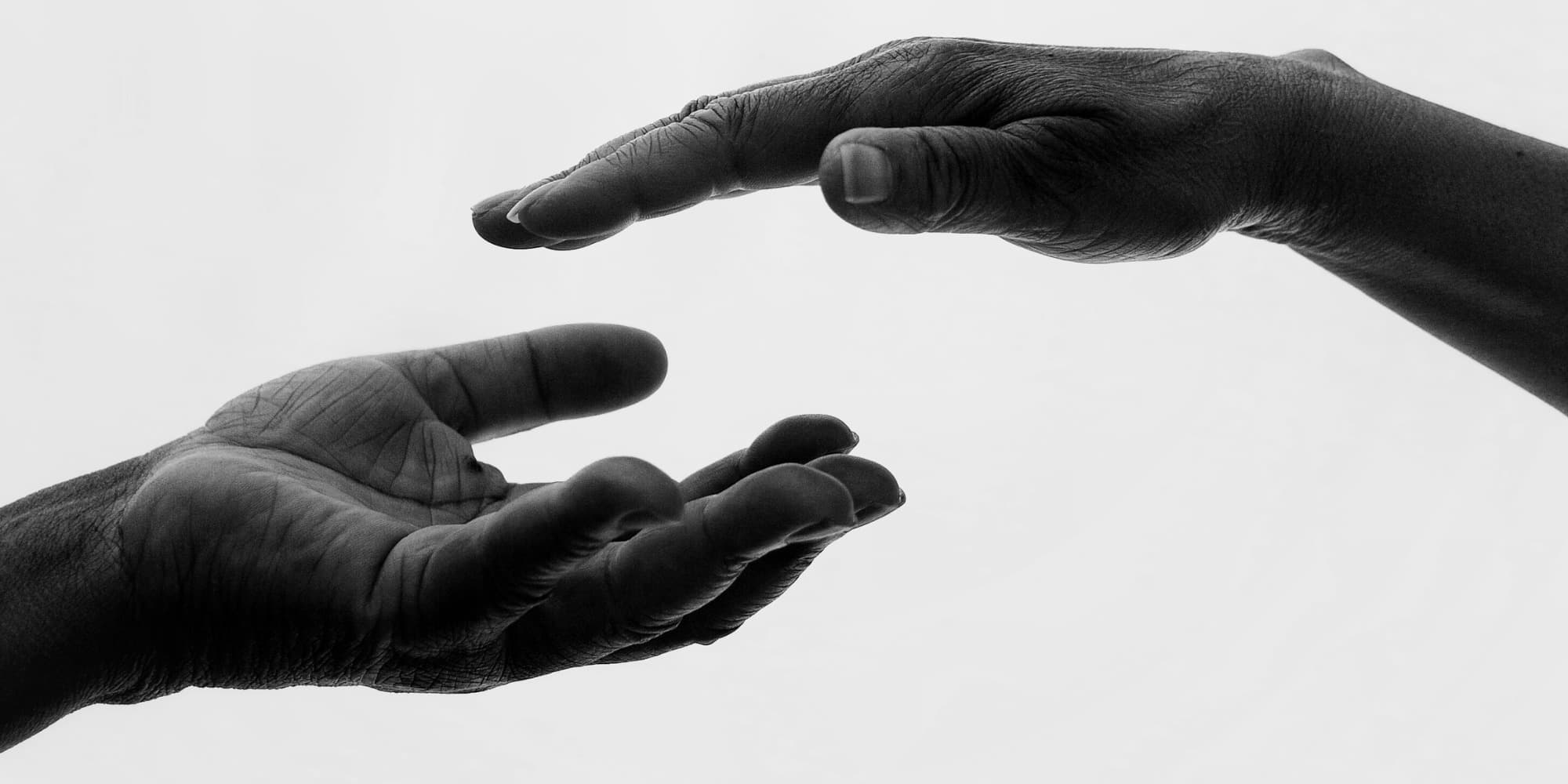 A black and white image of hands about to clasp. One hand turned up and the other is facing downwards, implying giving and receiving.