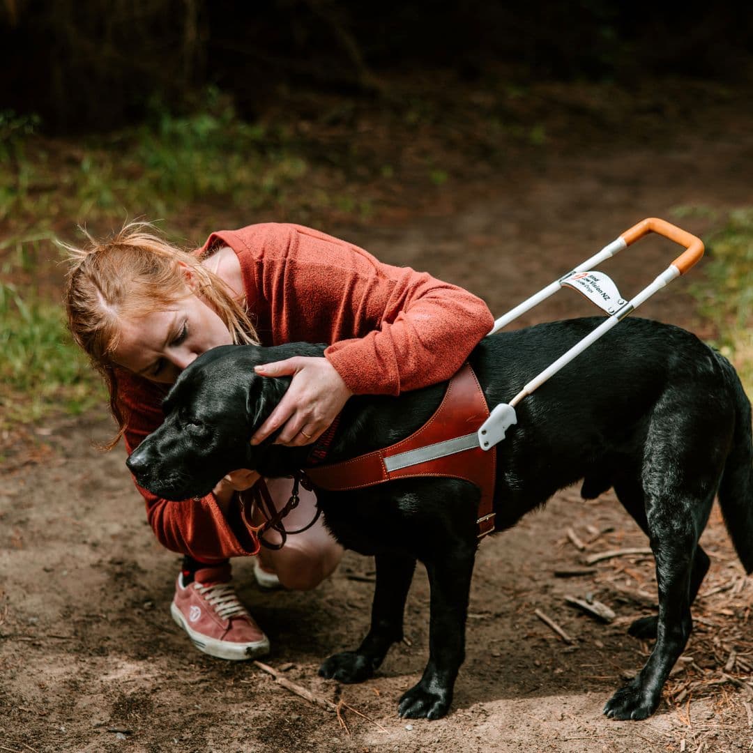 A women crouched down next to her guide dog, giving it a kiss.