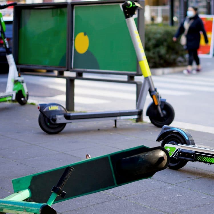 E-scooters parked next to a pedestrian crossing. One is lying on its side, blocking a footpath.