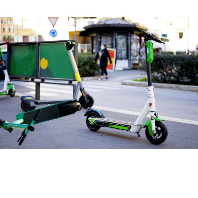 E-scooters parked next to a pedestrian crossing. One is lying on its side, blocking a footpath.