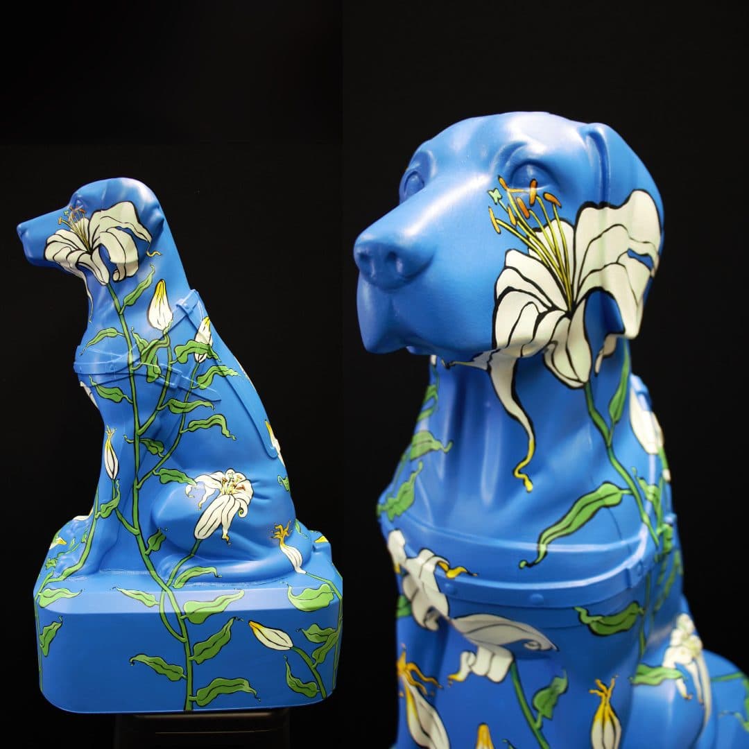A repurposed Blind Low Vision NZ Trudy dog decorated blue with white and yellow floral patterns against a black background.