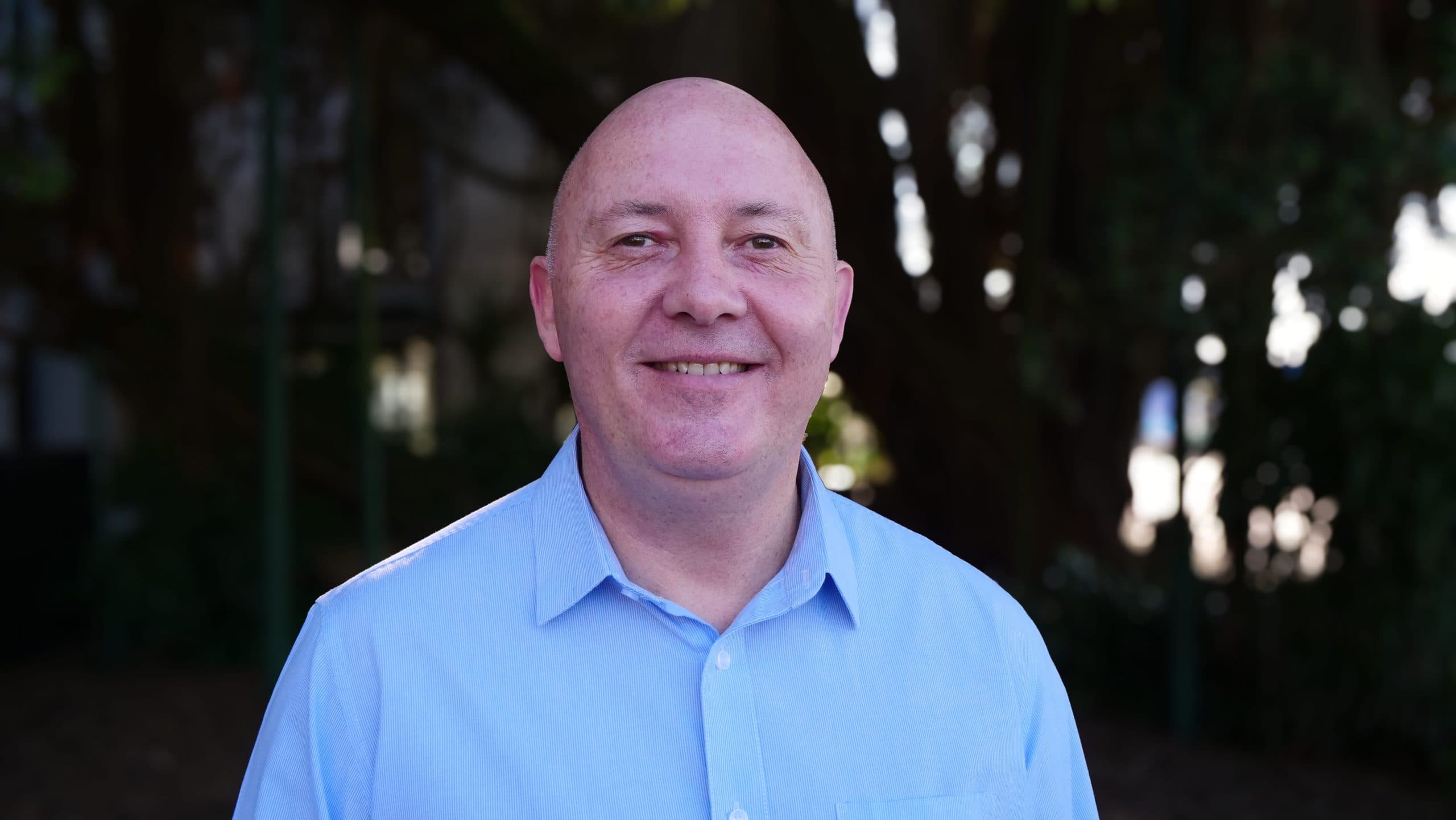 Blind Low Vision NZ CFO, Stephen Keeling, wearing a grey shirt smiles for the camera.