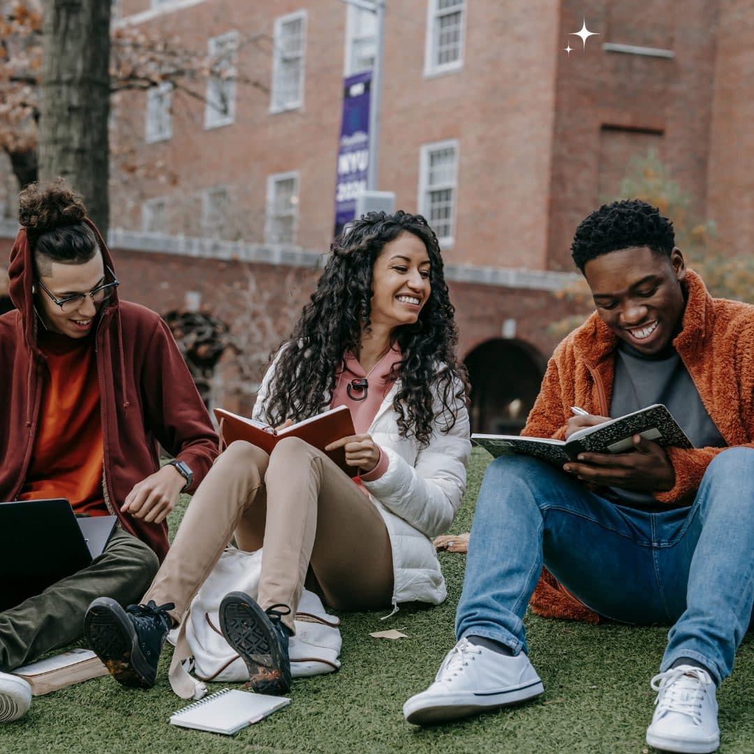 A female and two male students study outside at a university campus.