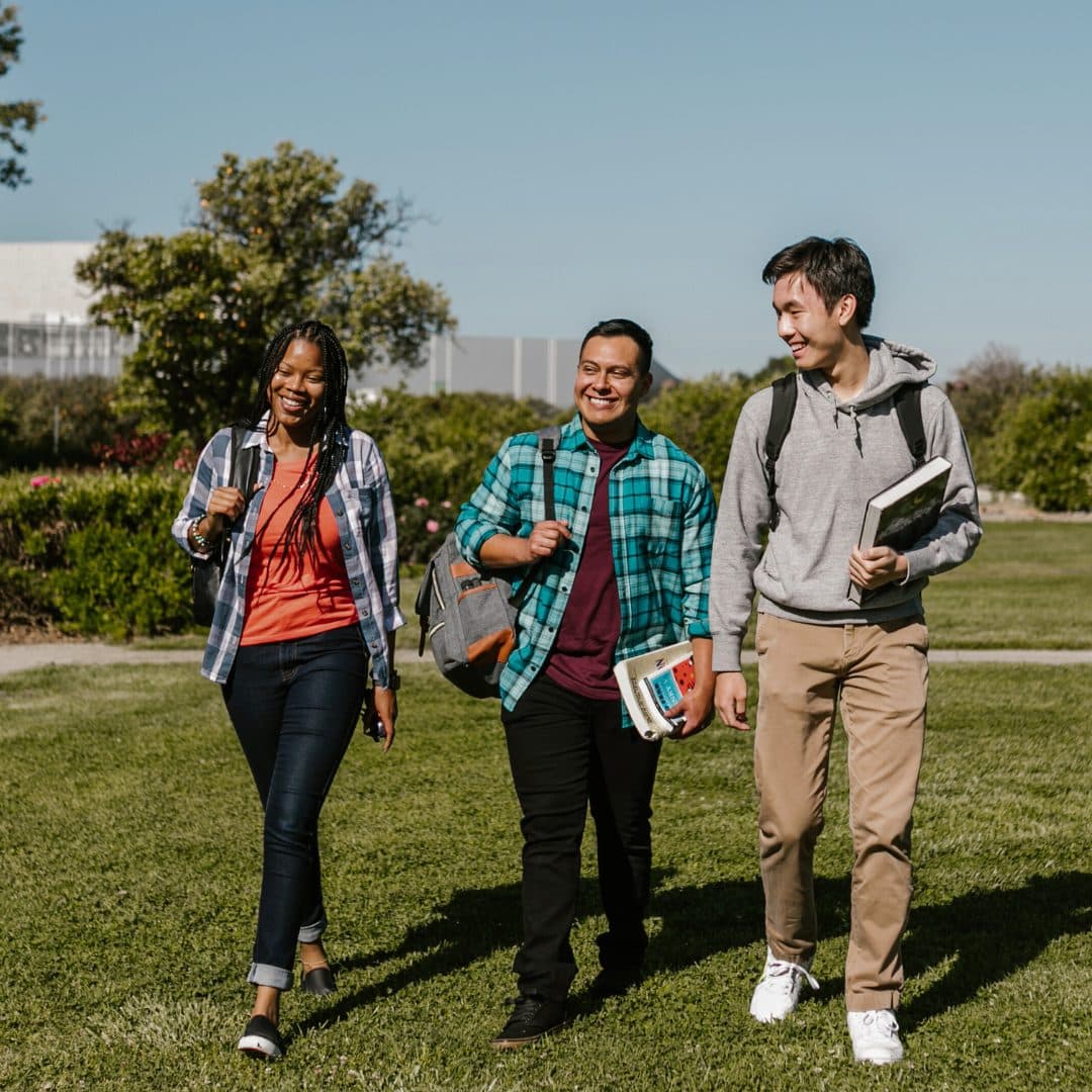 A female and two male students take a walk walk outside at a university campus.