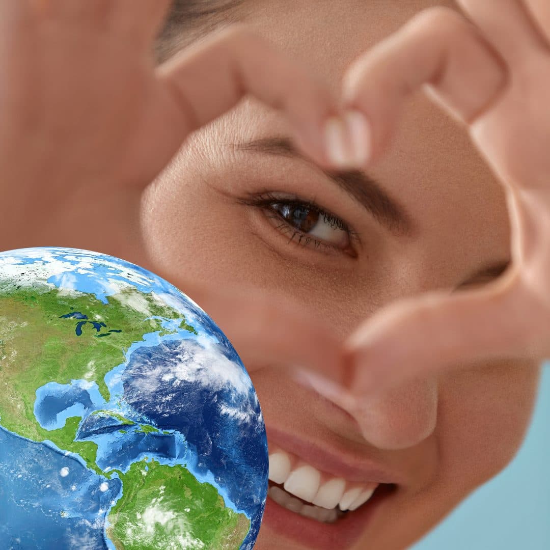 A woman making a heart shape with her hands, highlighting her eye, with a globe in the foreground