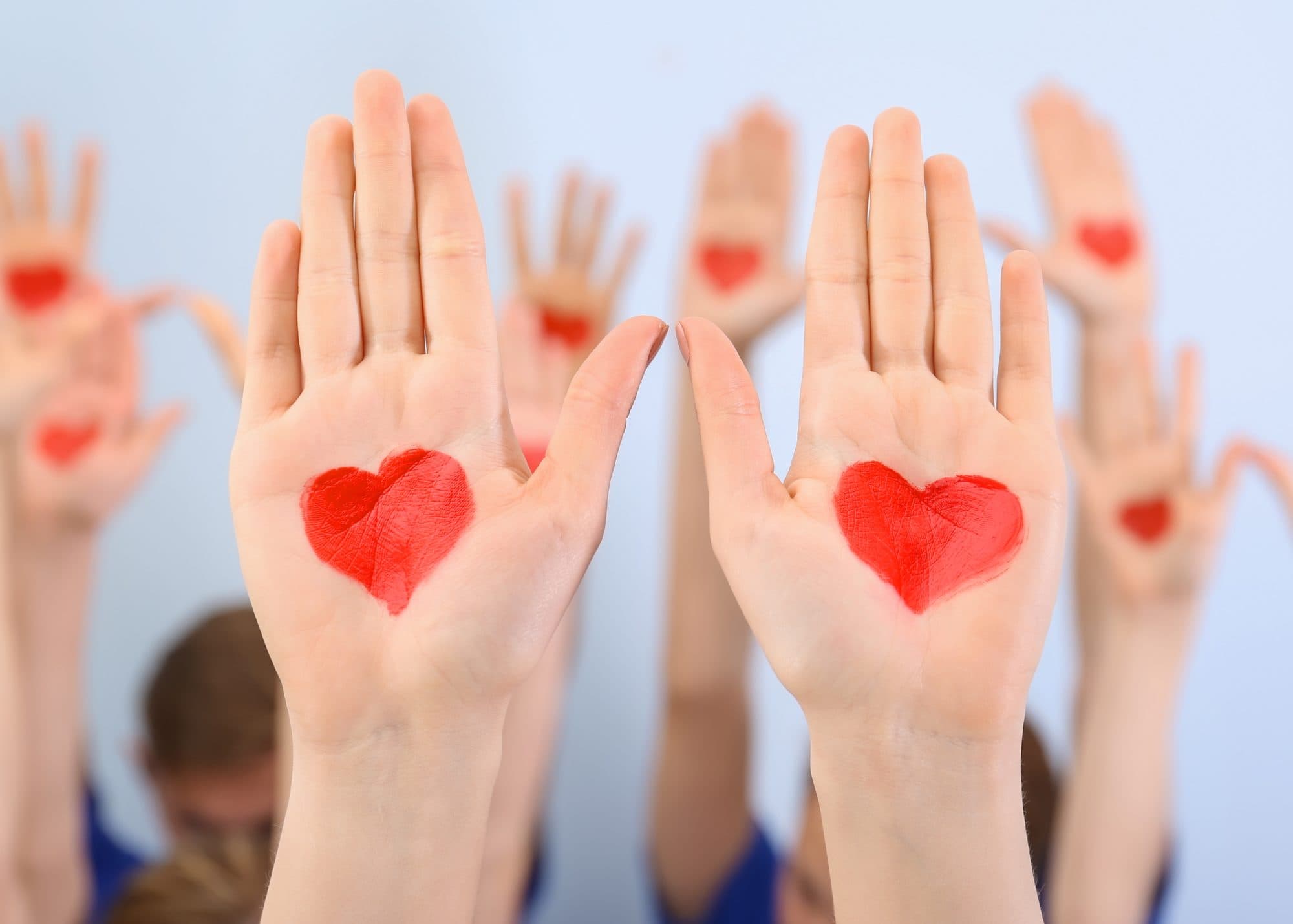 Image Description: A photo of peoples' raised hands with redhearts painted on them.