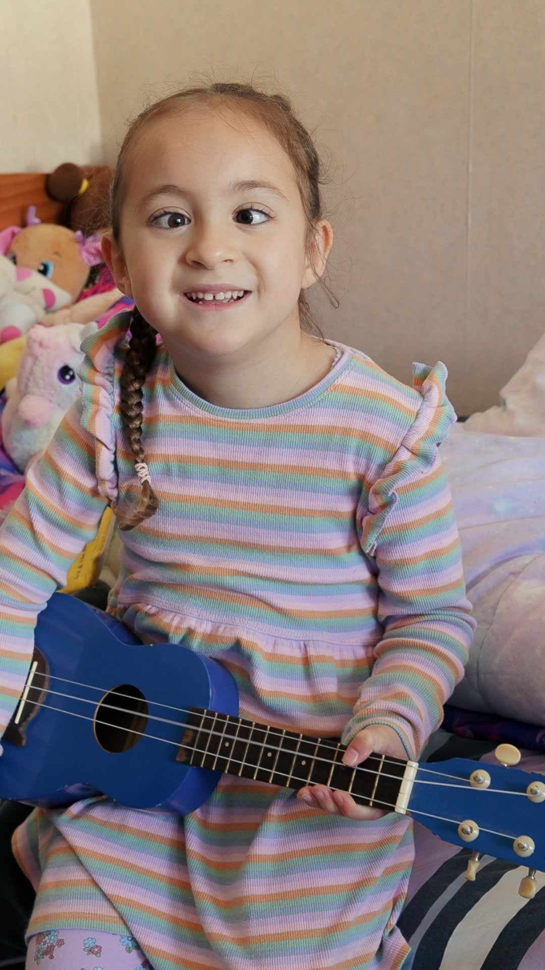 A young child sitting on her bed with a ukelele.