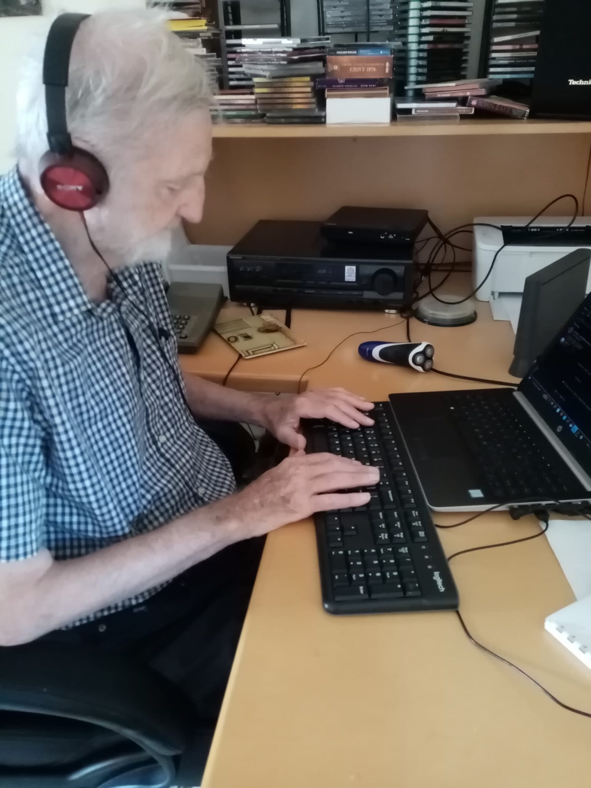 Allan is sitting at a desk on his computer. He is wearing headphones and typing on his keyboard.