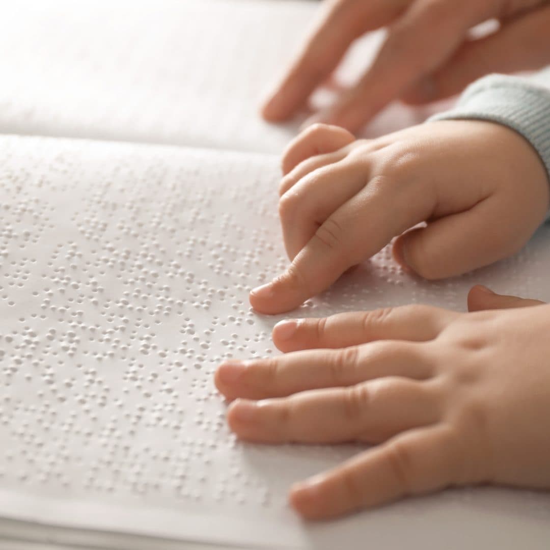 A child's and an adult's hands touching a page with Braille on it.