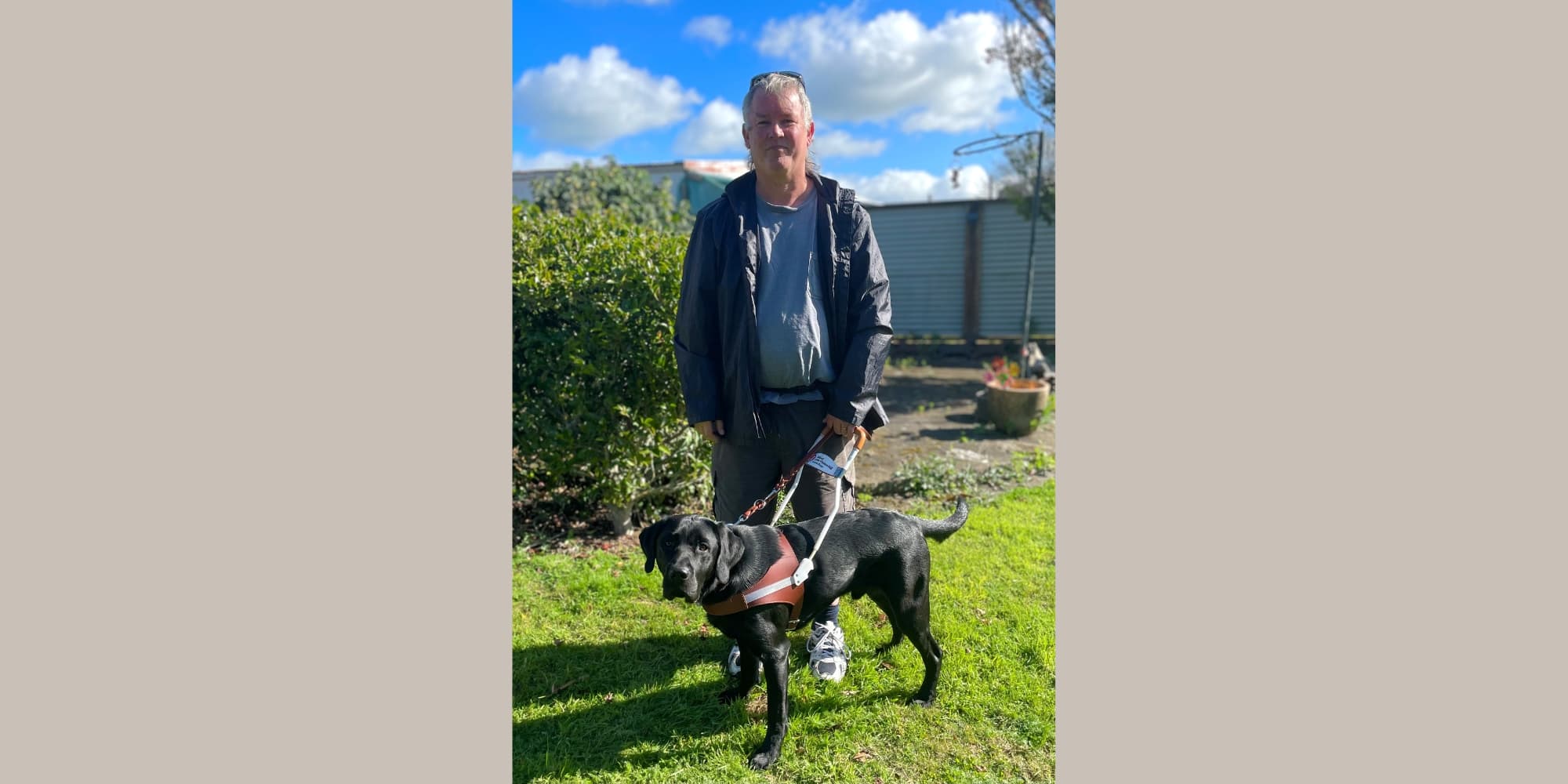 Gene, and his black labrador Orion standing together at Orion's graduation. Gene is holding Orion by his harness.