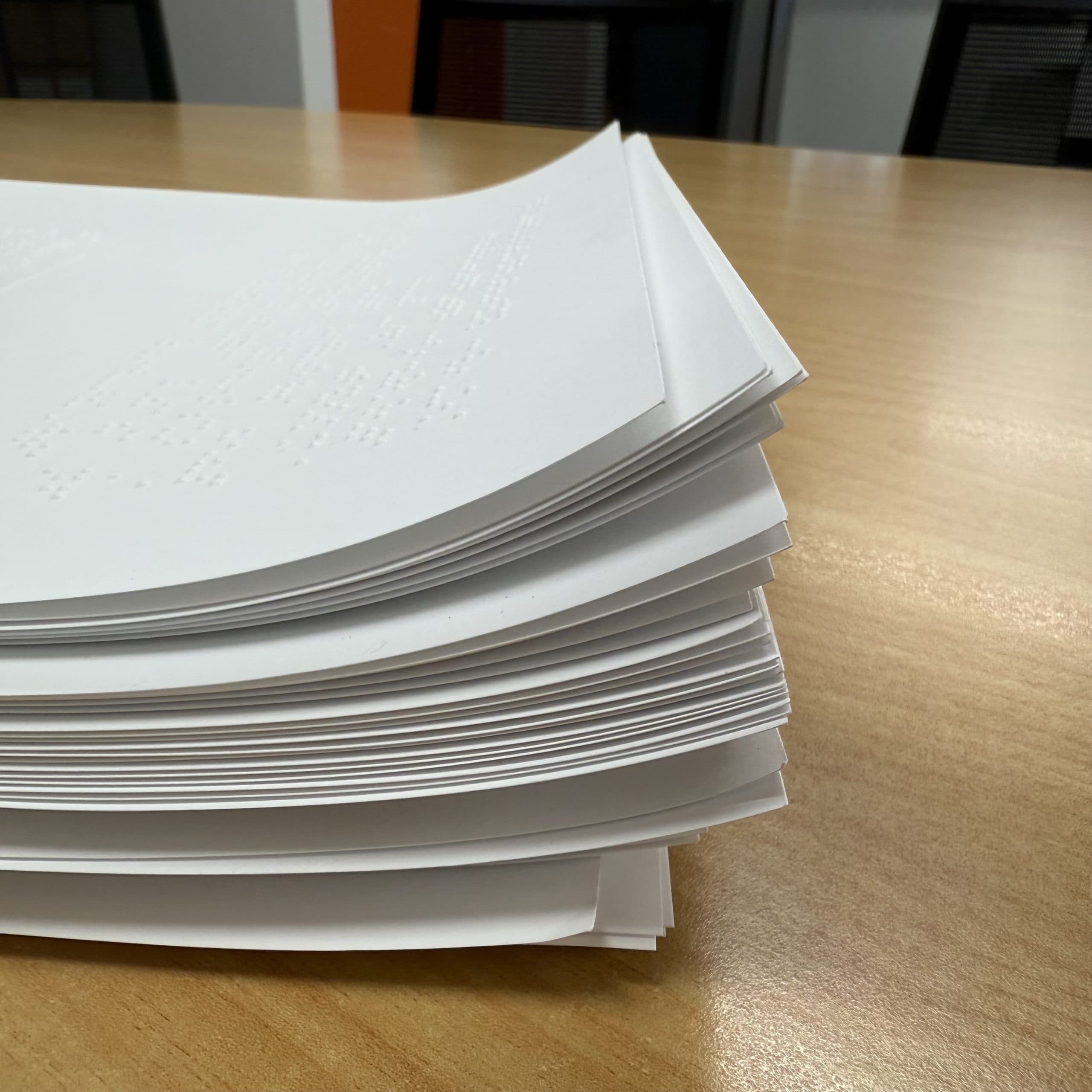 Stacks of white pages of Braille text on a table.