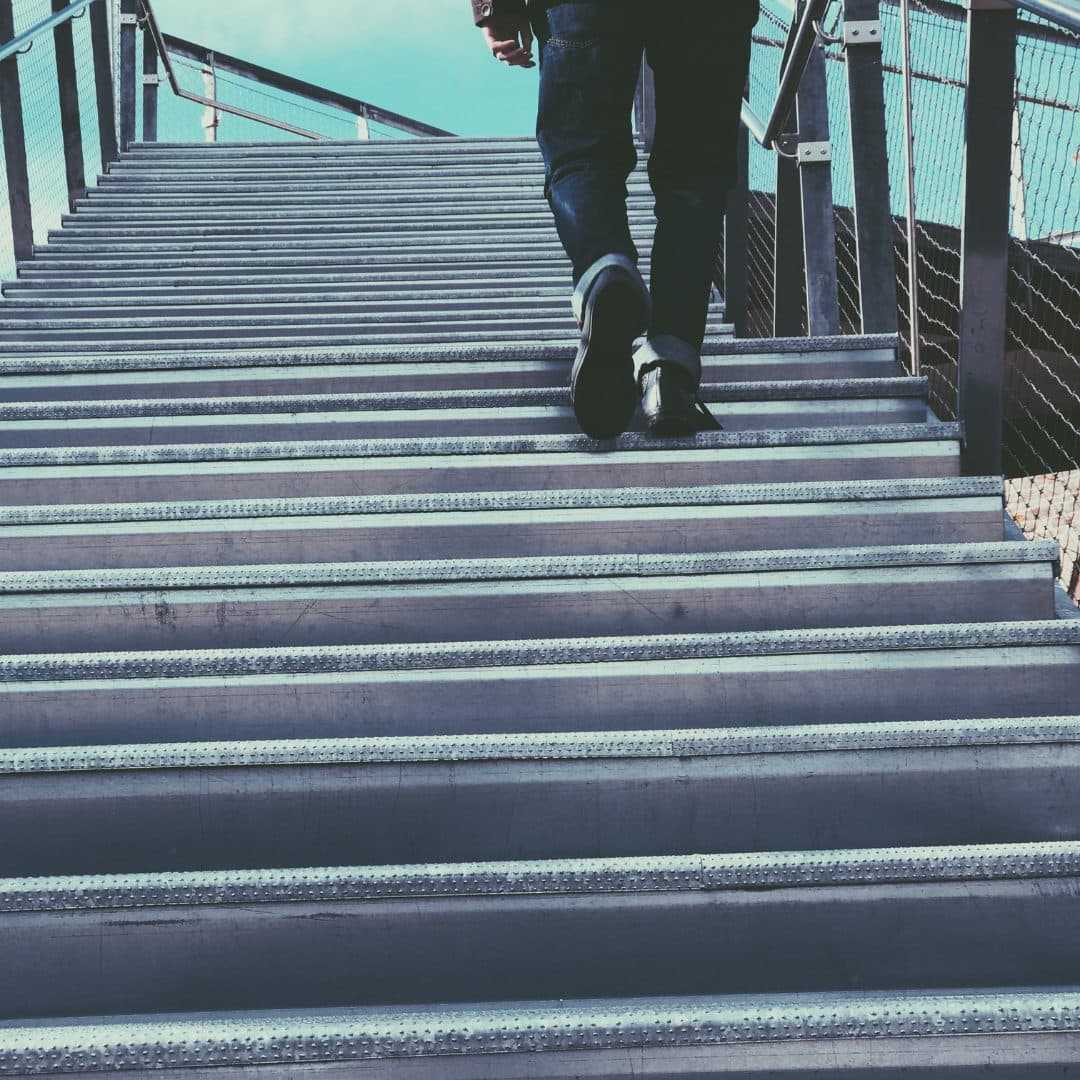 Stairs leading up to an outdoor space, featuring the legs of someone walking up them.