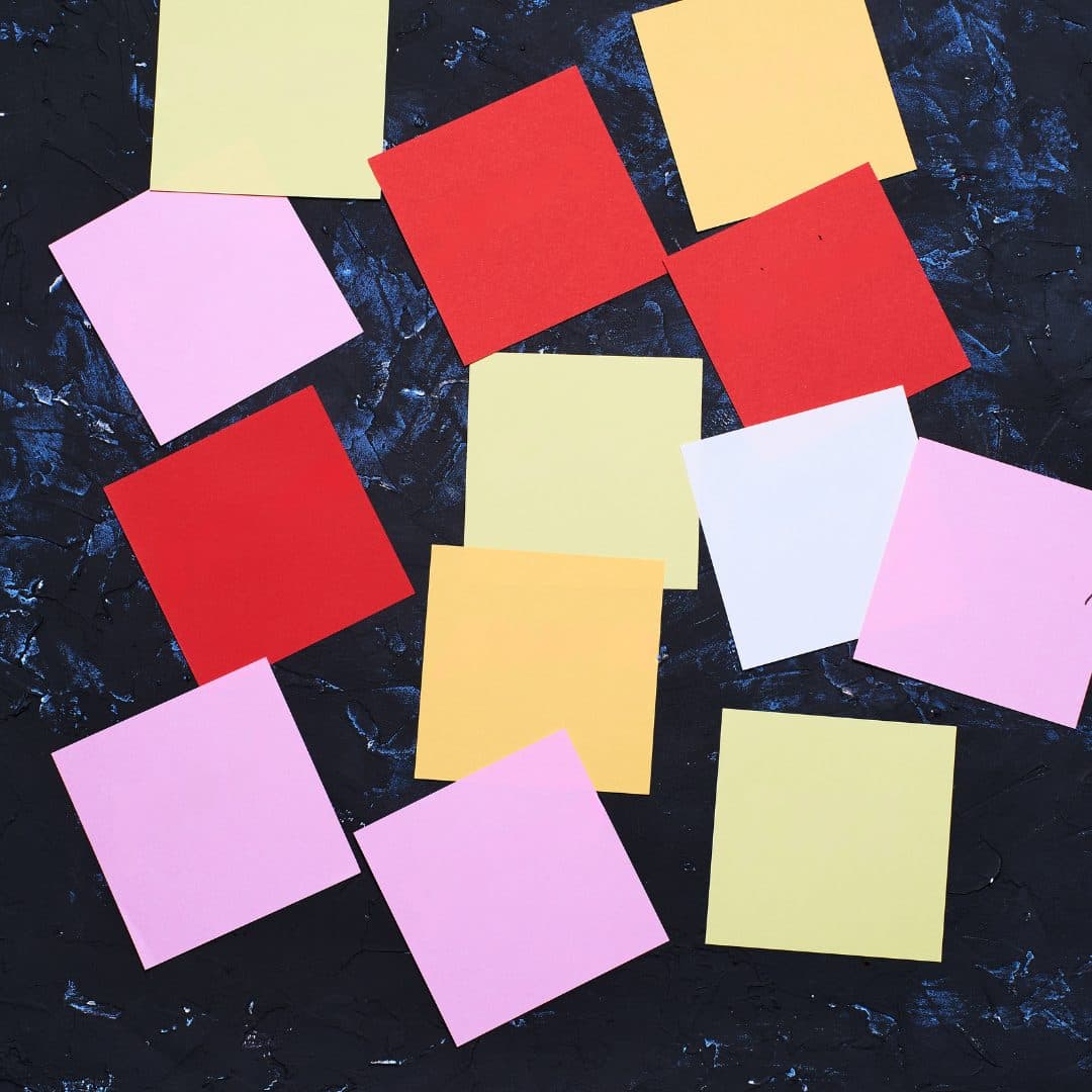 Multiple square pieces of paper of different colours on a dark blue surface.