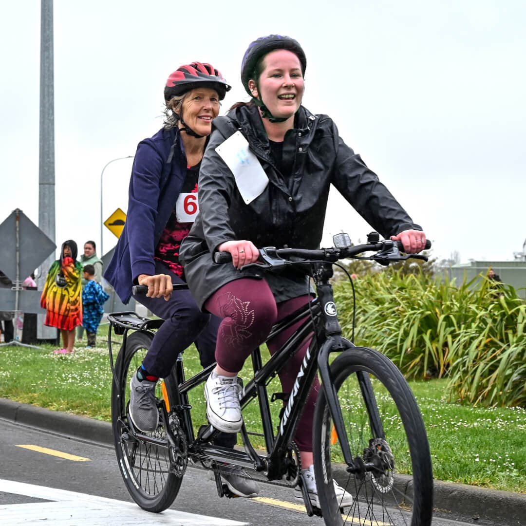 Two ladies riding a tandem bike on the street