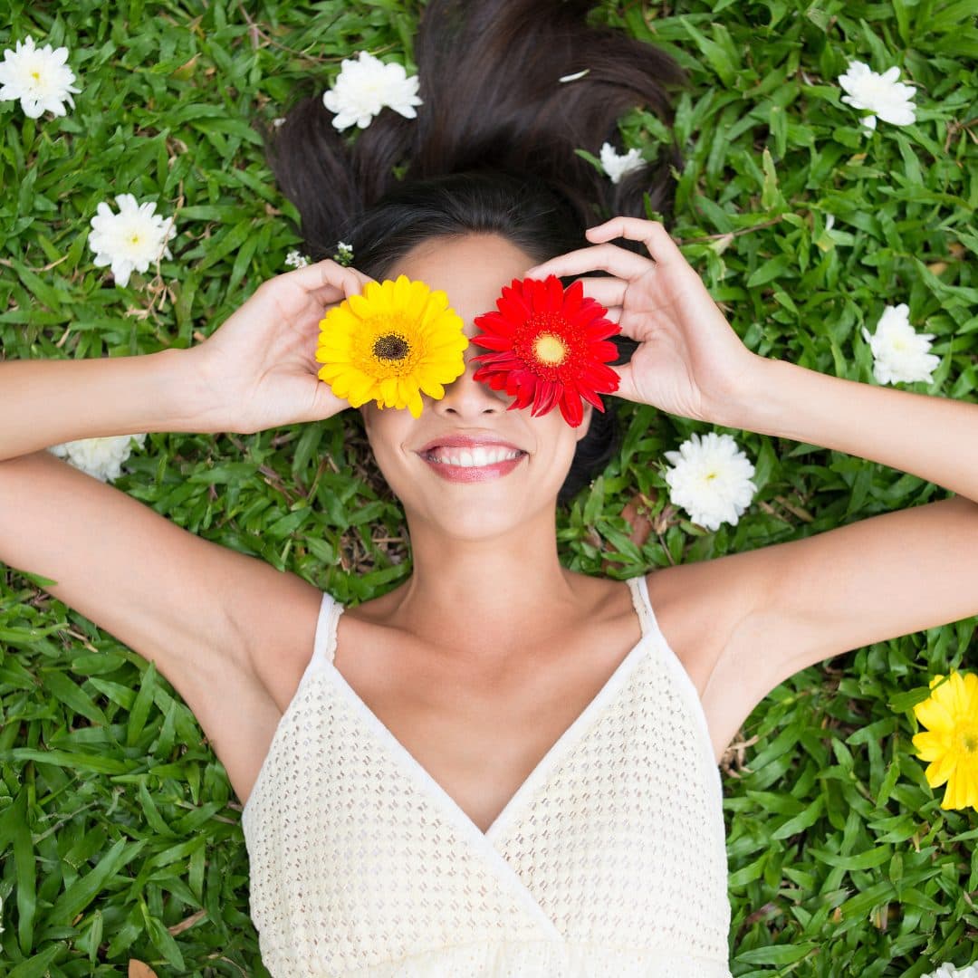 A woman laying on the grass with flowers in her eyes.