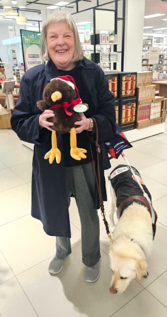 Carolyn and Zeb are out shopping. Carolyn is holding a stuffed toy, and Zeb is wearing his black harness
