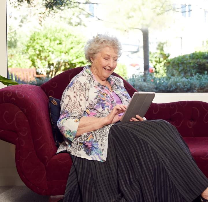 Client Jenny sits on a comfortable looking sofa and reads using her tablet