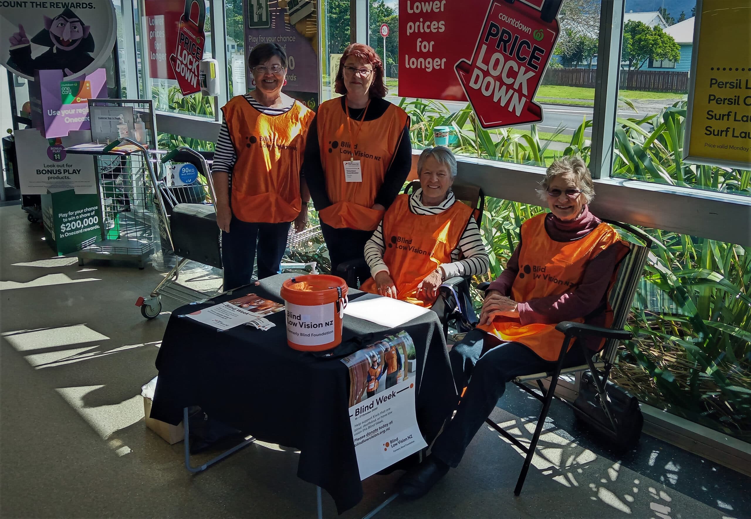 A group of fundraising volunteers are gathered around a table to collect for Blind Low Vision NZ