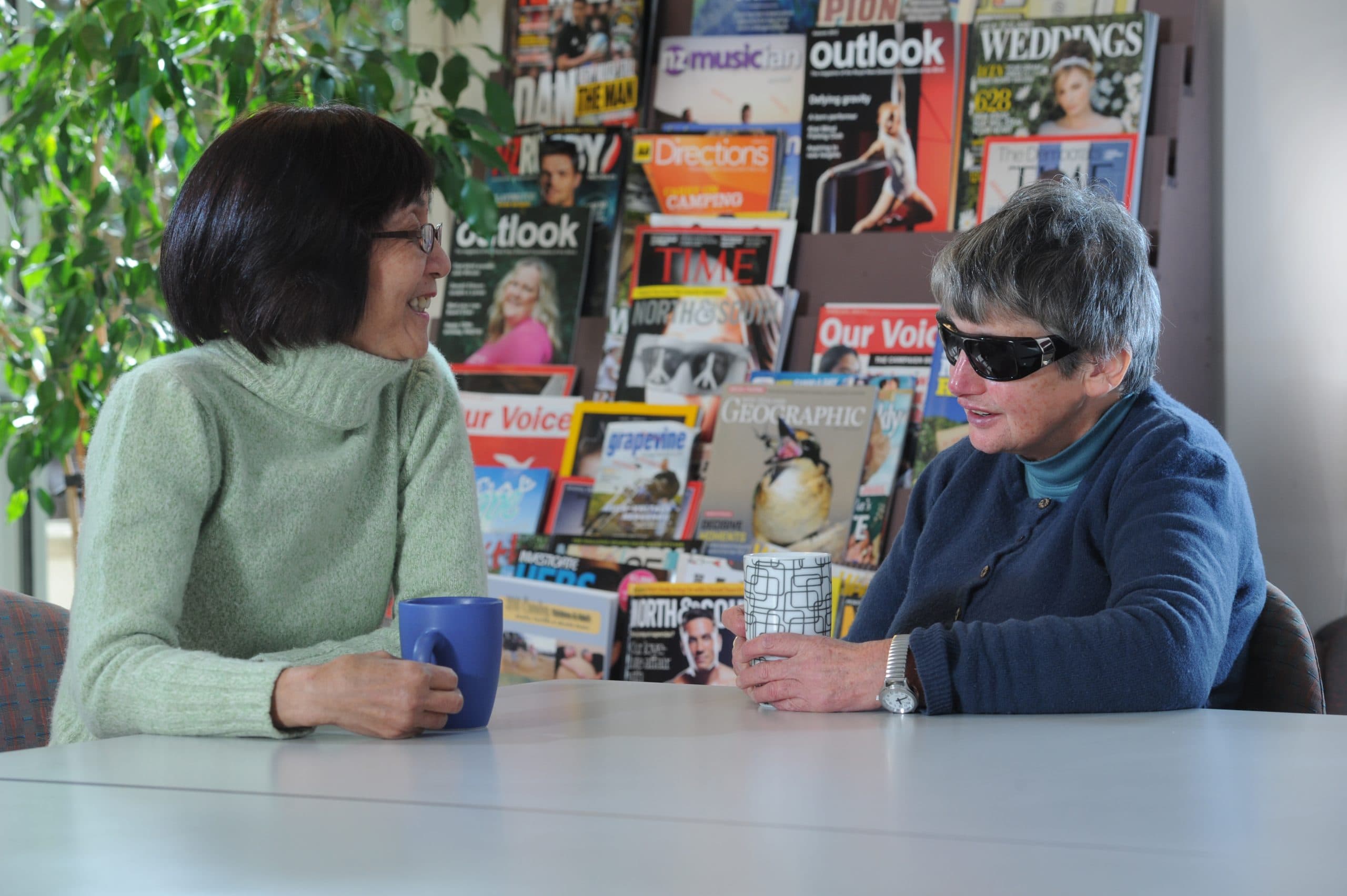 Two clients of Blind Low Vision NZ talking on a table