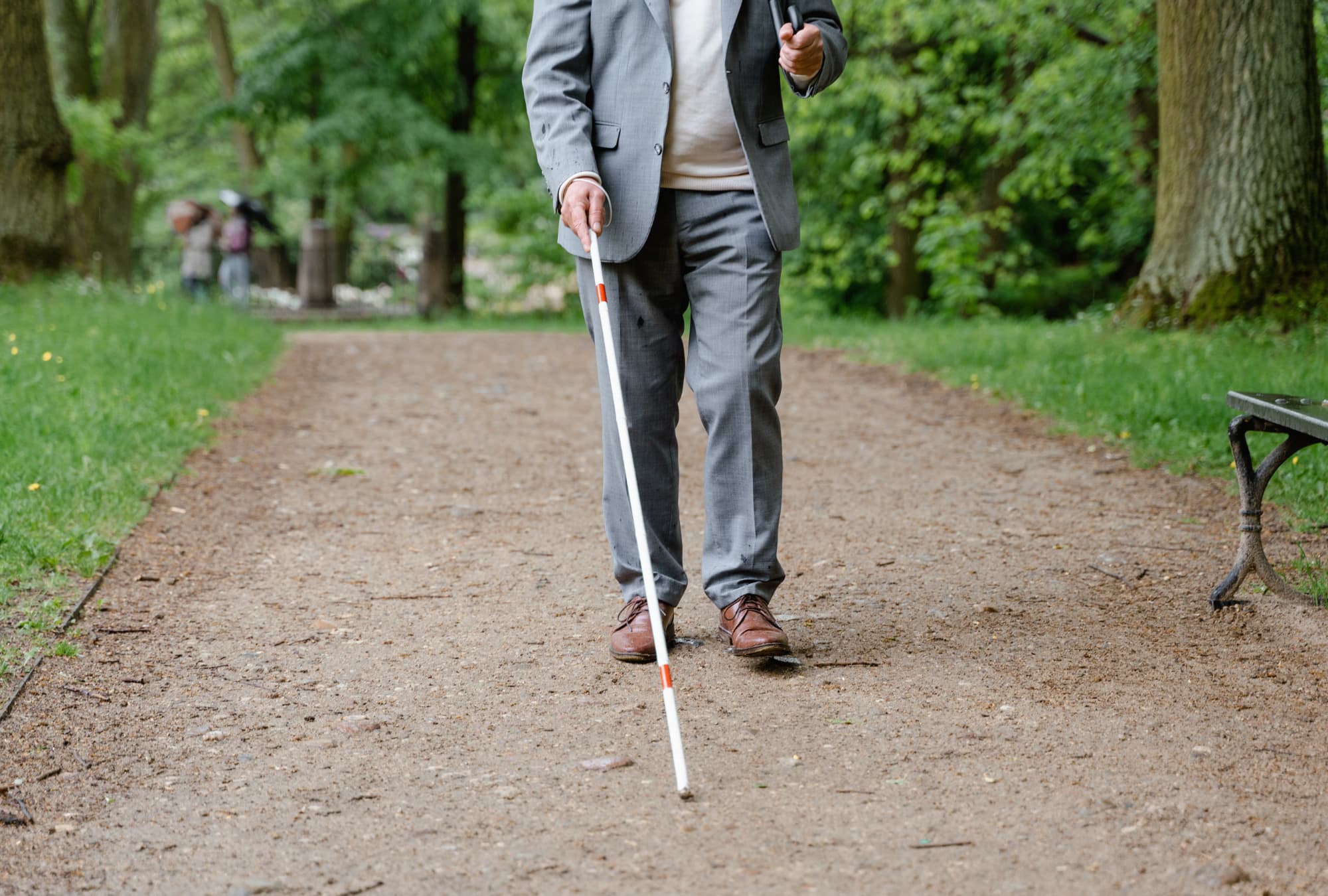 A person who is blind or has low vision walking around a park with his white cane