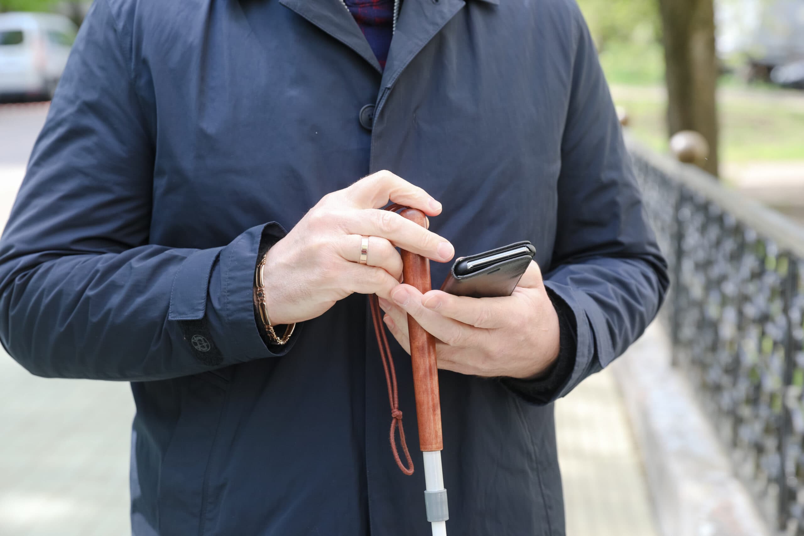 A man is outside, holding his white cane and phone in his hands