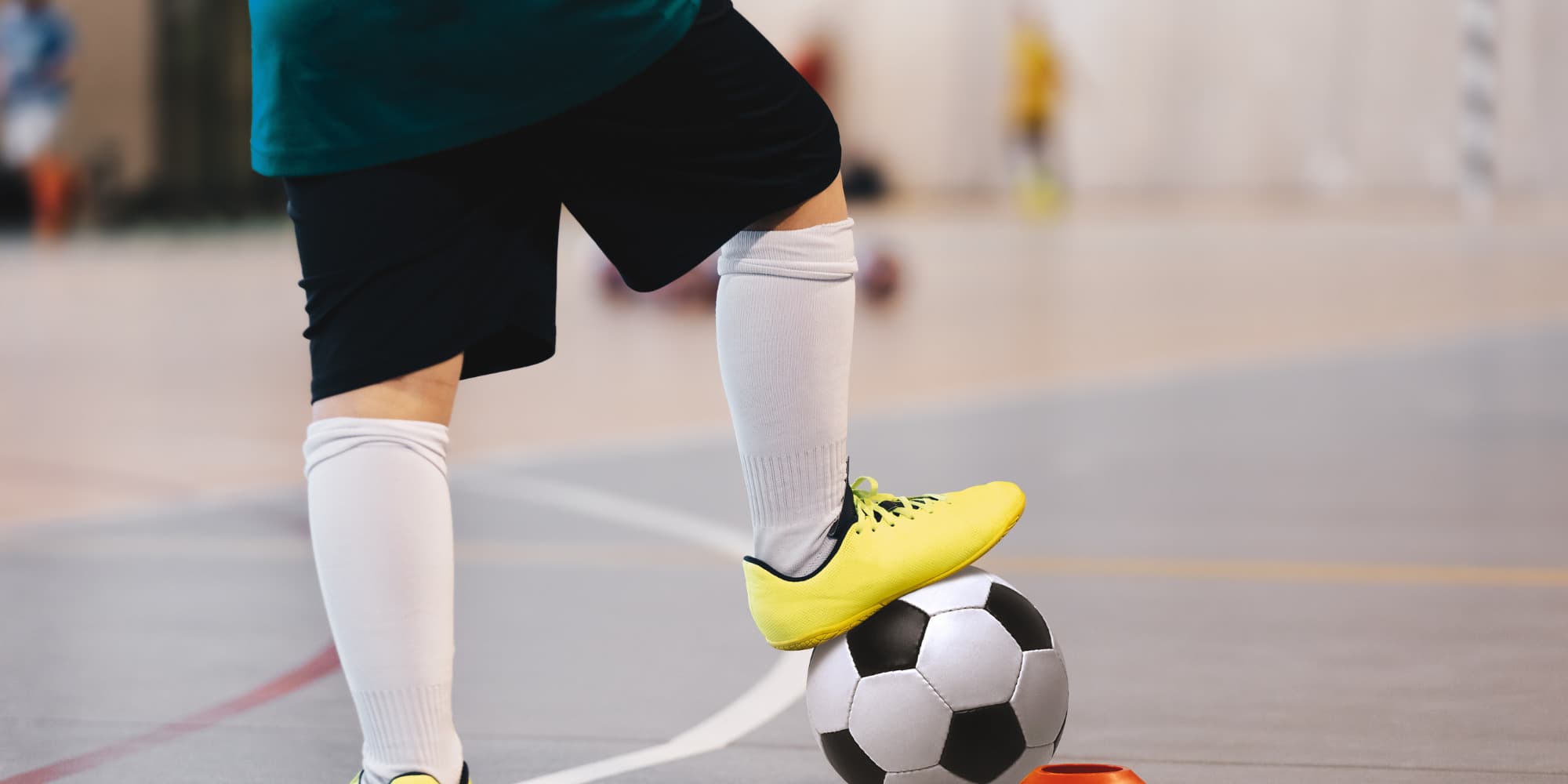 A pair of legs with one foot on a soccer ball on an indoor court
