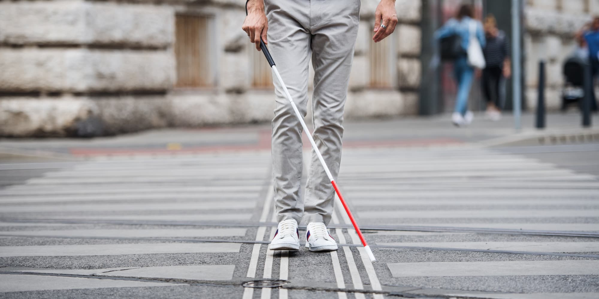 A shot from the waist down of a man navigating a city footpath with a white cane.