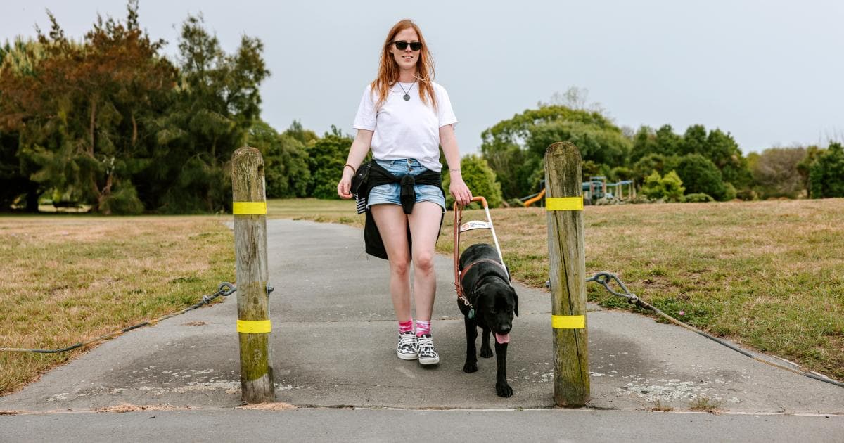 A photo of Blind Low Vision member, Laura with her guide dog Ryder walking outdoors.
