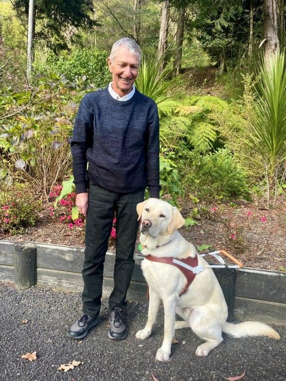 Brian standing next to a his guide dog Flynn, a yellow Labrador wearing a harness.