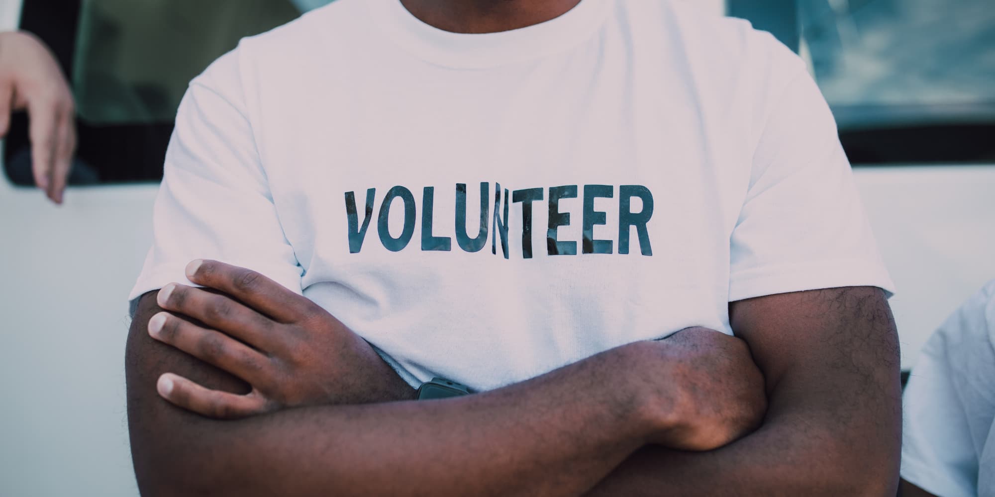 A close up of a male volunteer crossing his arms with his t-shirt focused in on the word "Volunteer" printed on it.