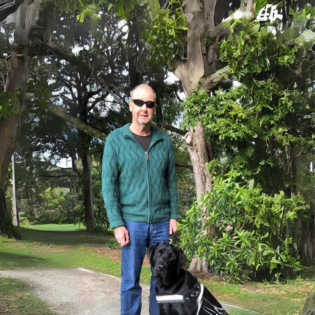 Steve with his guide dog Archie beside him. They're outside at the park, facing the camera.